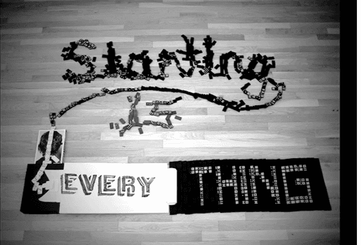 A black and white photo of a domino game that forms the text: Starting is Every Thing.