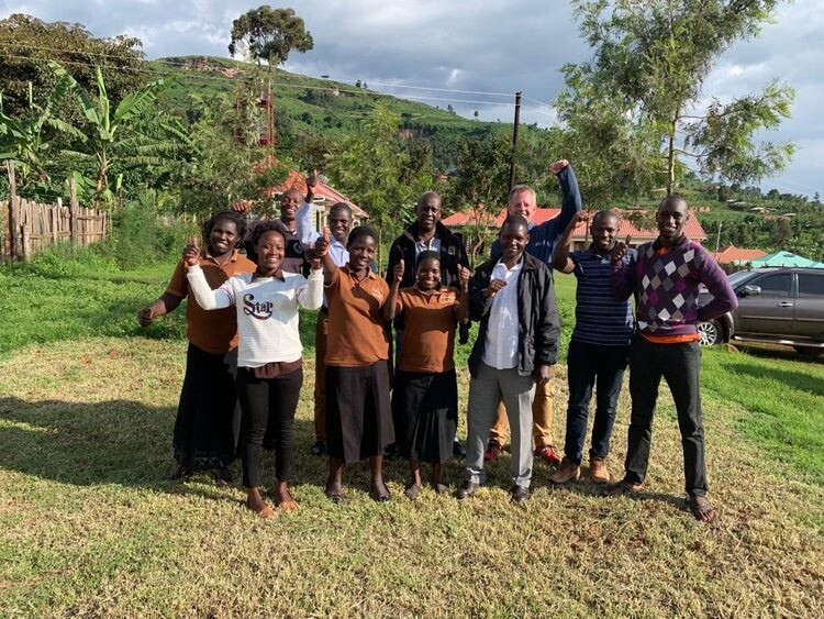 A large group of people posing together outdoors in front of a hillside and guest houses.