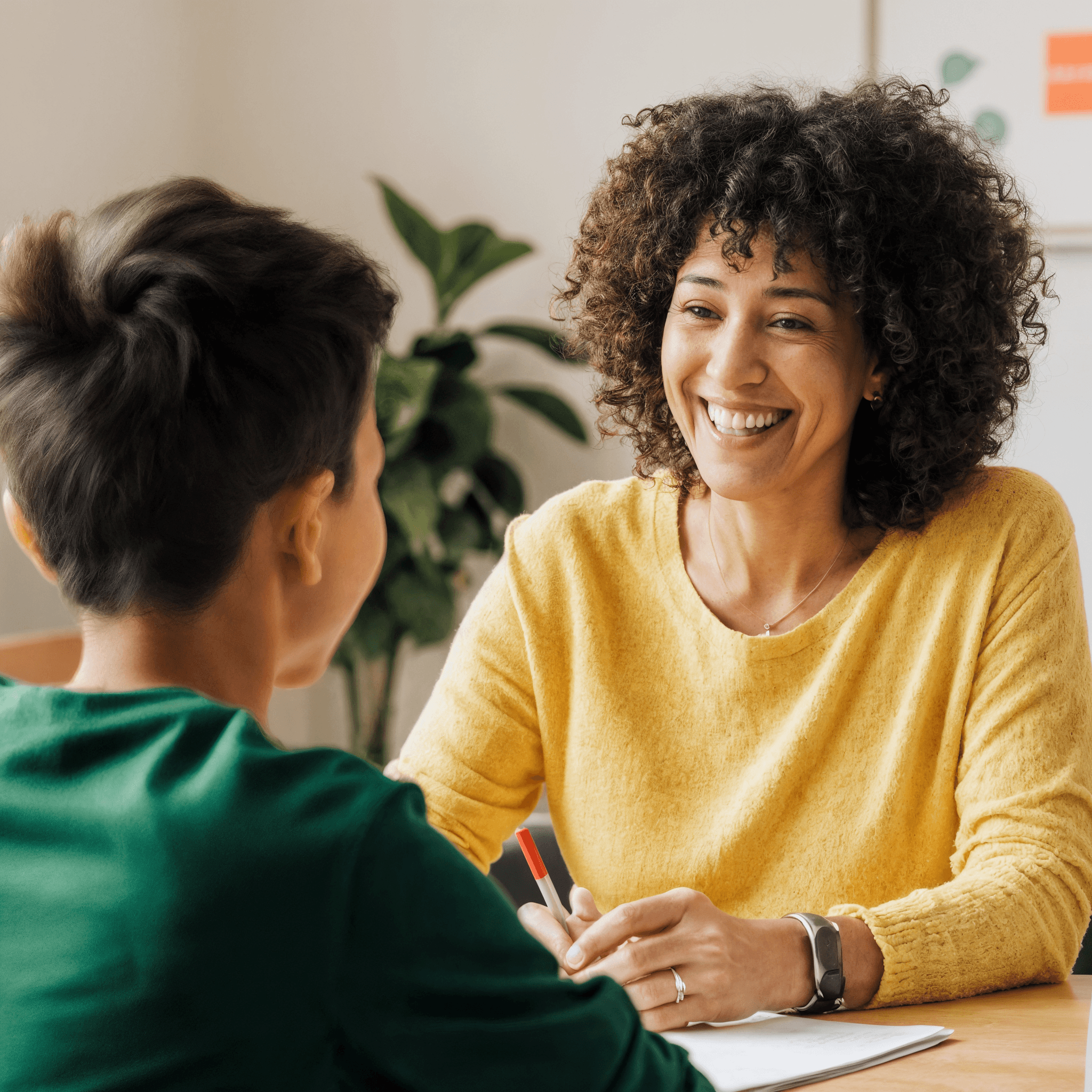 Teacher smiling at a student during a tutoring session in a bright classroom.
