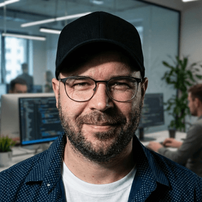 Smiling young man with short hair poses against a dark background, wearing a green button-up shirt.