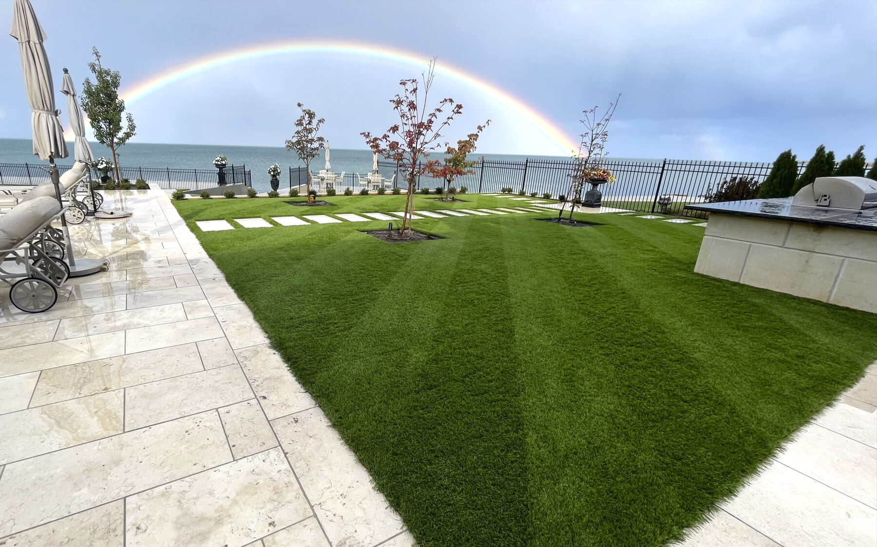 A vibrant rainbow arches over a cozy backyard provided by AGL Grass, adding color to the serene outdoor space.