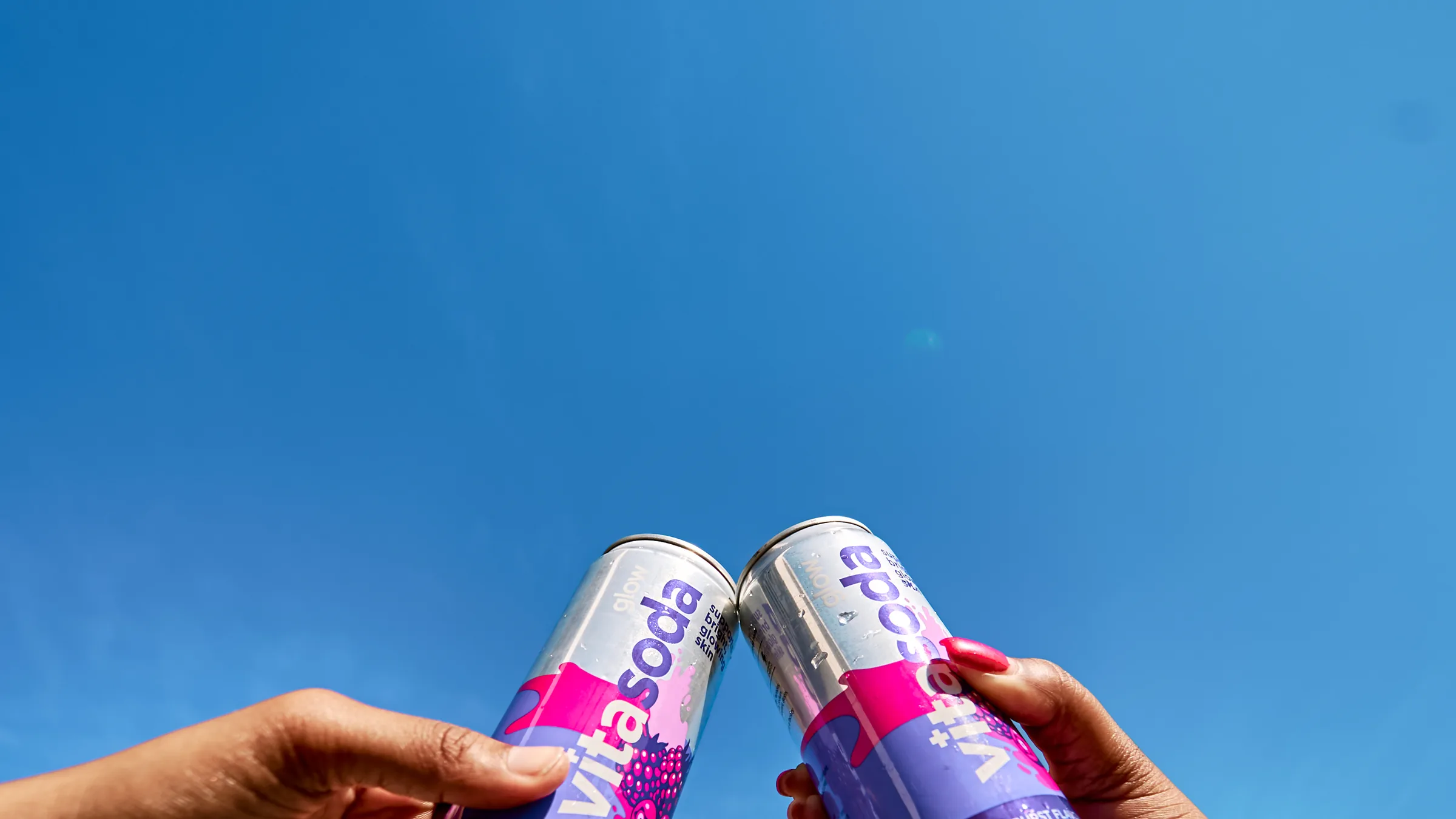 Two cans of Vita Soda Glow touched together against a blue sky