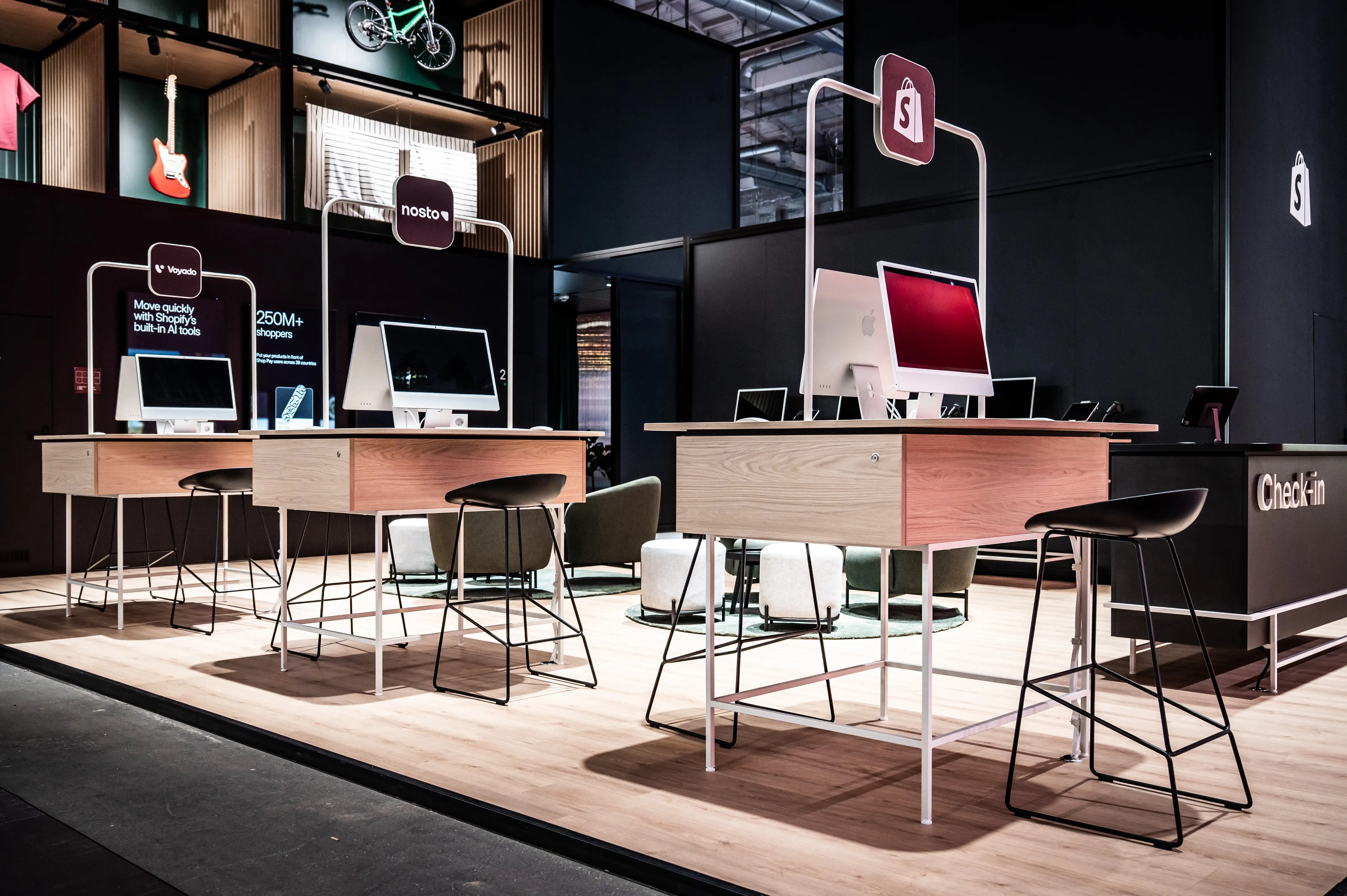 Wooden demo desks with iMacs, green chairs and Shopify signs inside the dark booth.