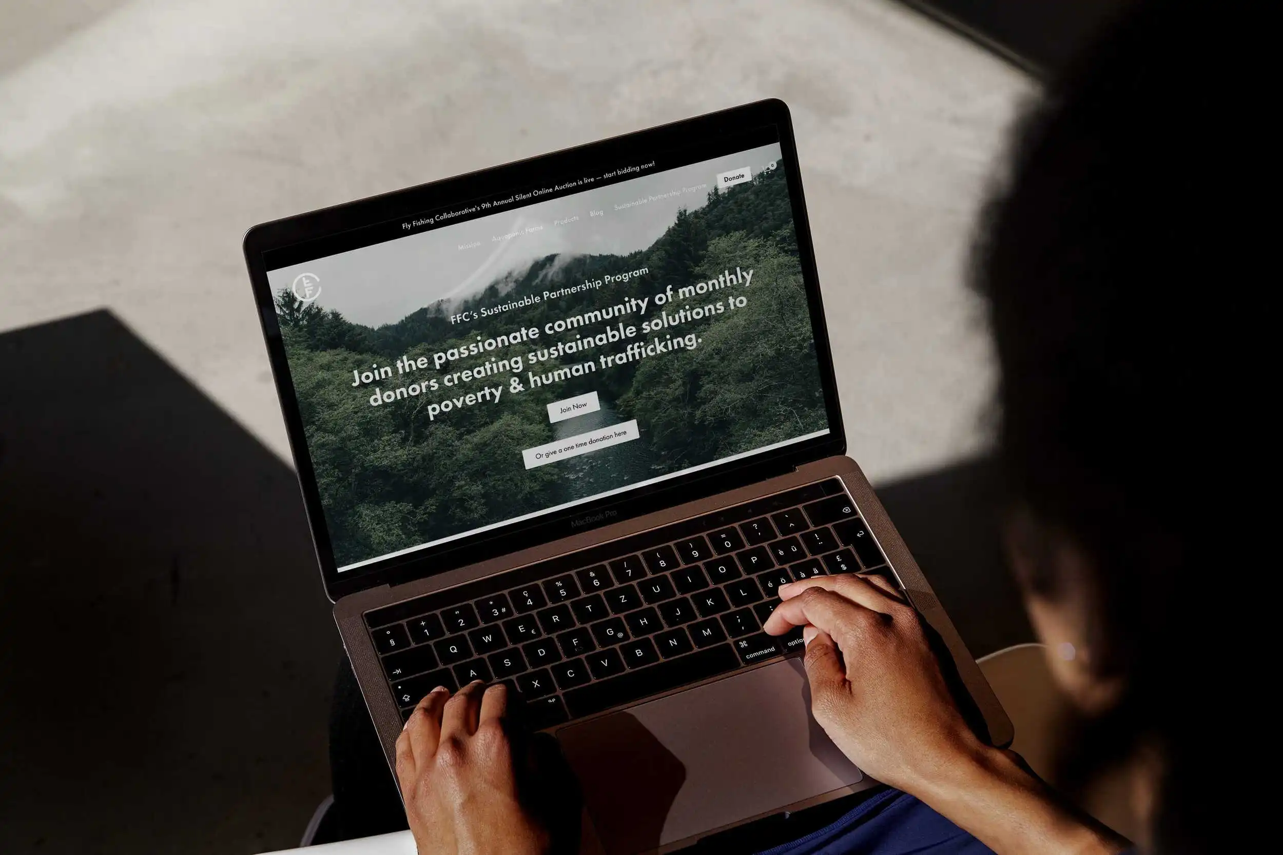 Laptop screen shows website about fighting poverty and human trafficking with a scenic background.