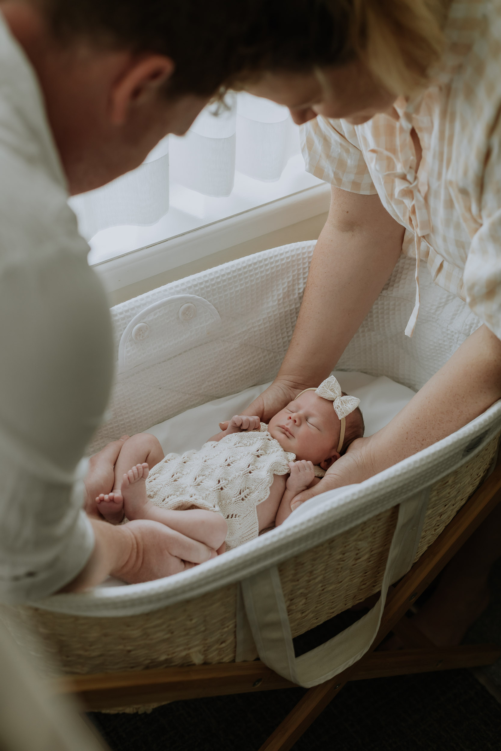 Parents holding newborn baby in basinet near window in Mackay