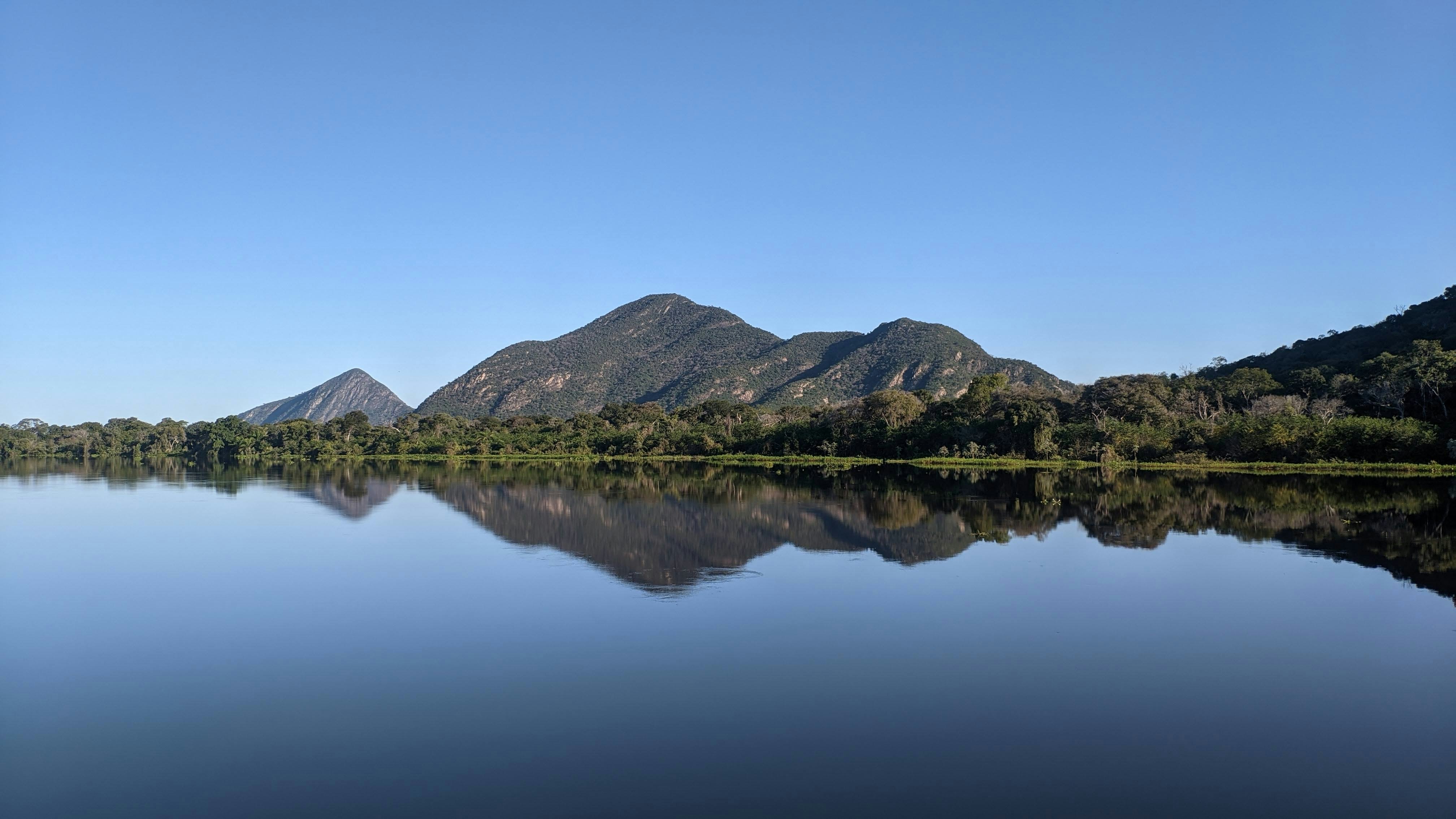 Spiegelung der Serra do Amolar im ruhigen Wasser des Rio Paraguai im West-Pantanal – beeindruckende Berglandschaft und dichter Wald unter wolkenlosem Himmel.