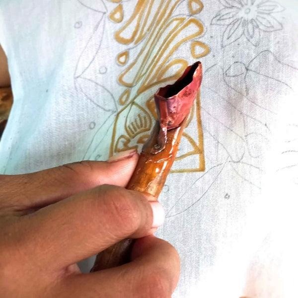 Artisan hand-applying batik wax resist technique — tjanting tool on fabric.
