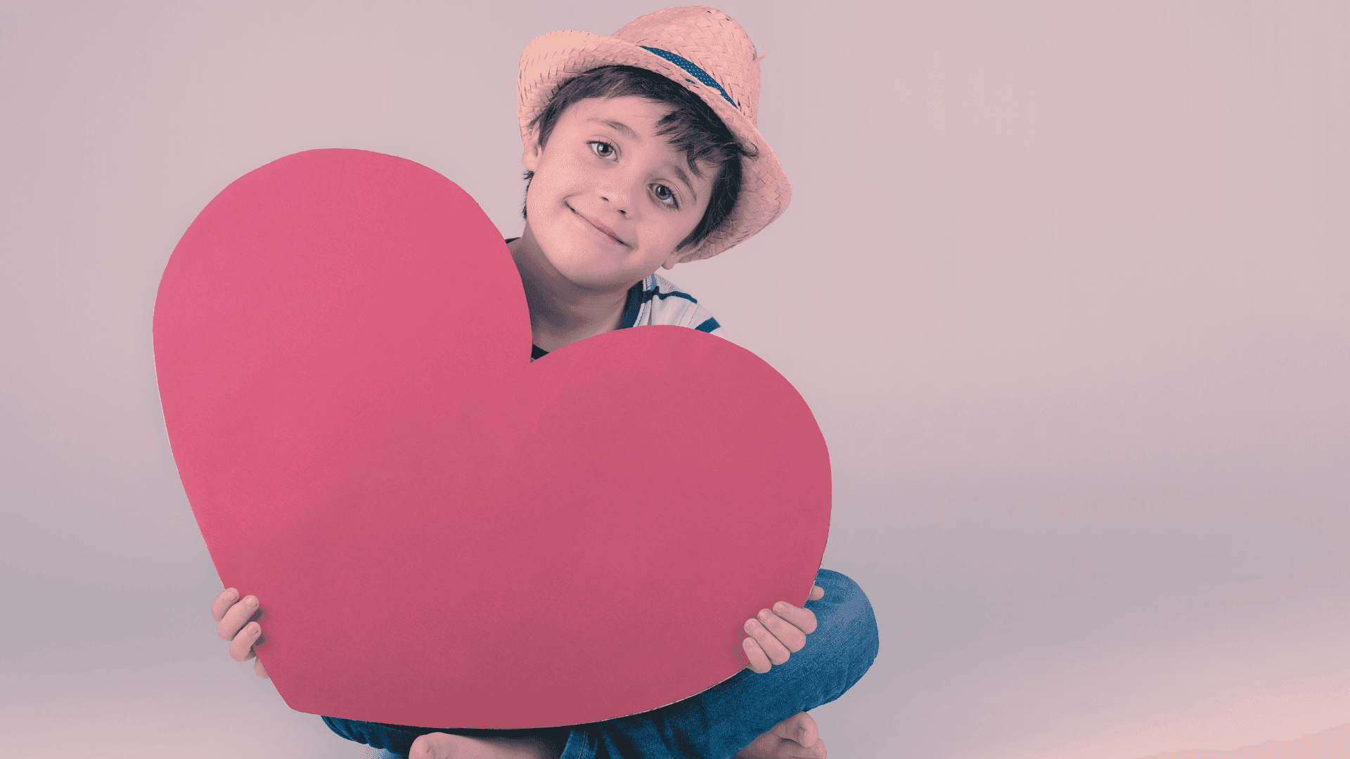 A young boy with a hat on holding a giant reed heart smiling twoards the camera