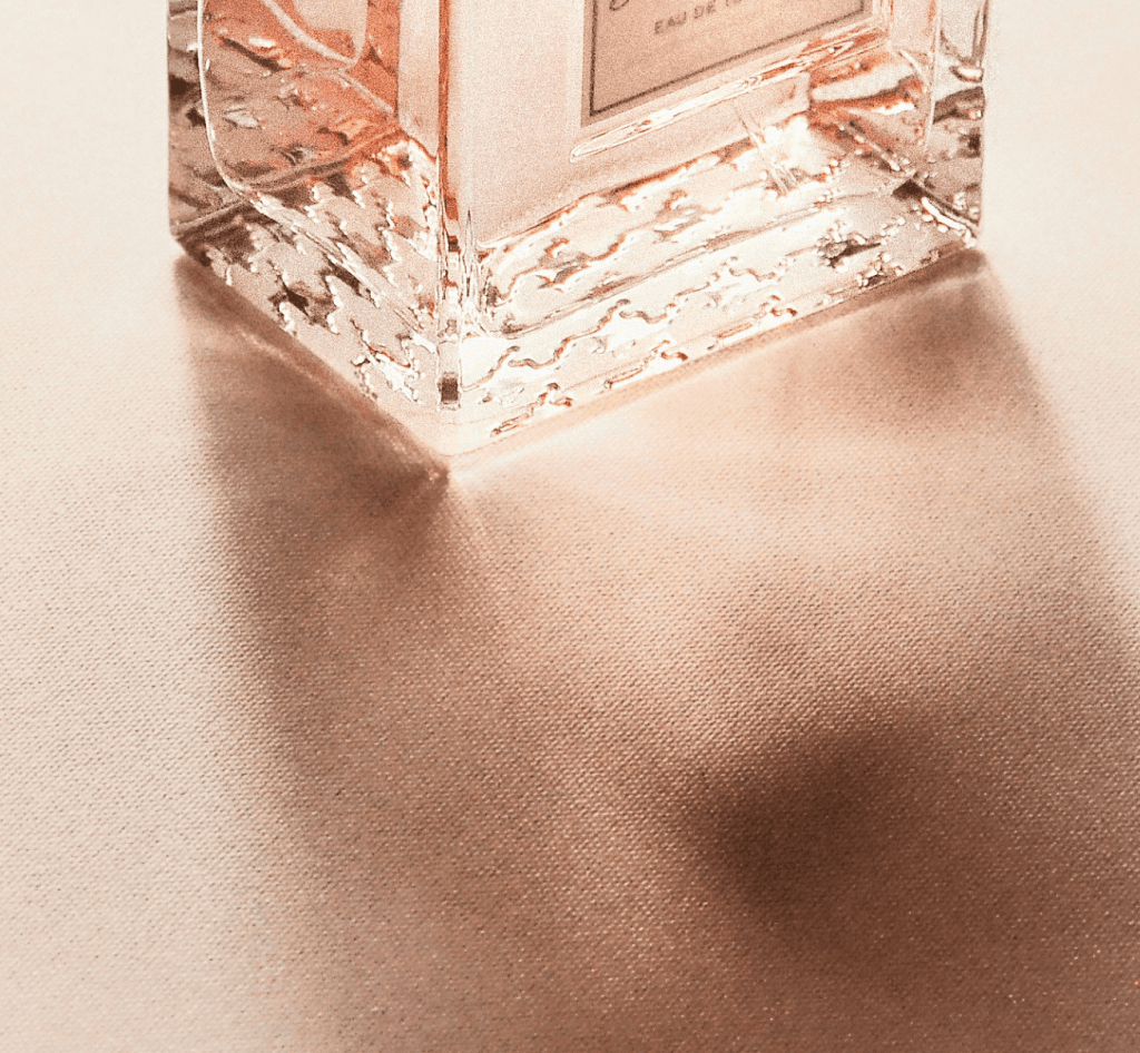 photo montrant le bas d'une bouteille de parfum, traversée par la lumière, son ombre portée sur un textile