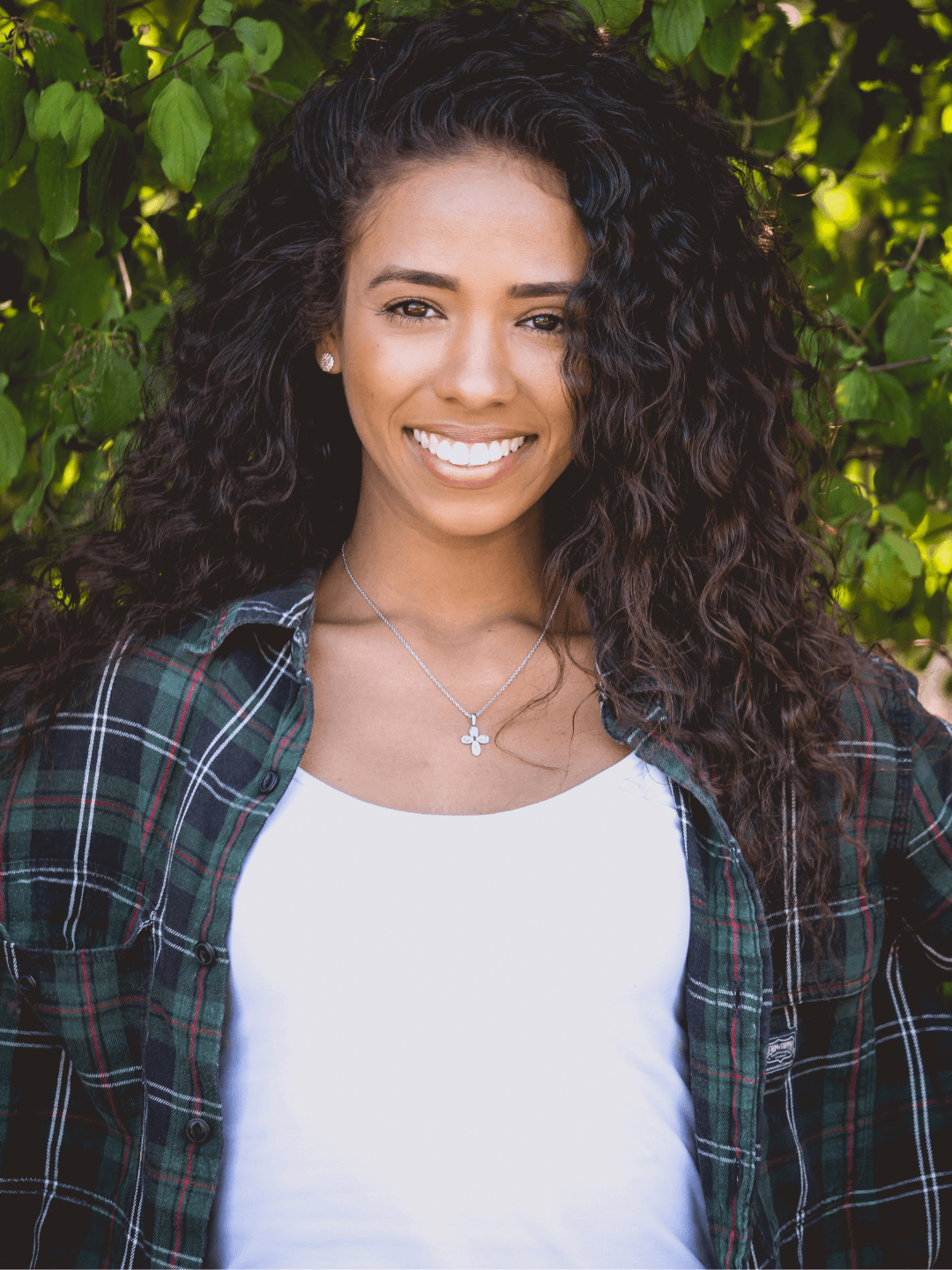 Portrait of a woman smiling at the camera in front of a what seems to be a green garden