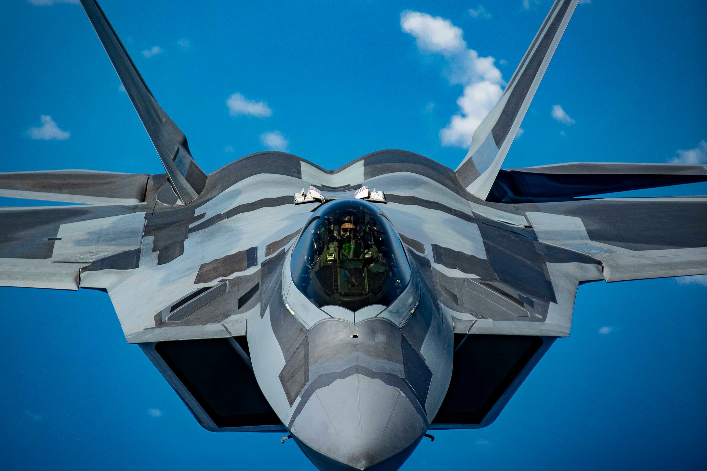 Close-up view of a stealth fighter jet in flight, with a visible cockpit and angular design against a clear blue sky.