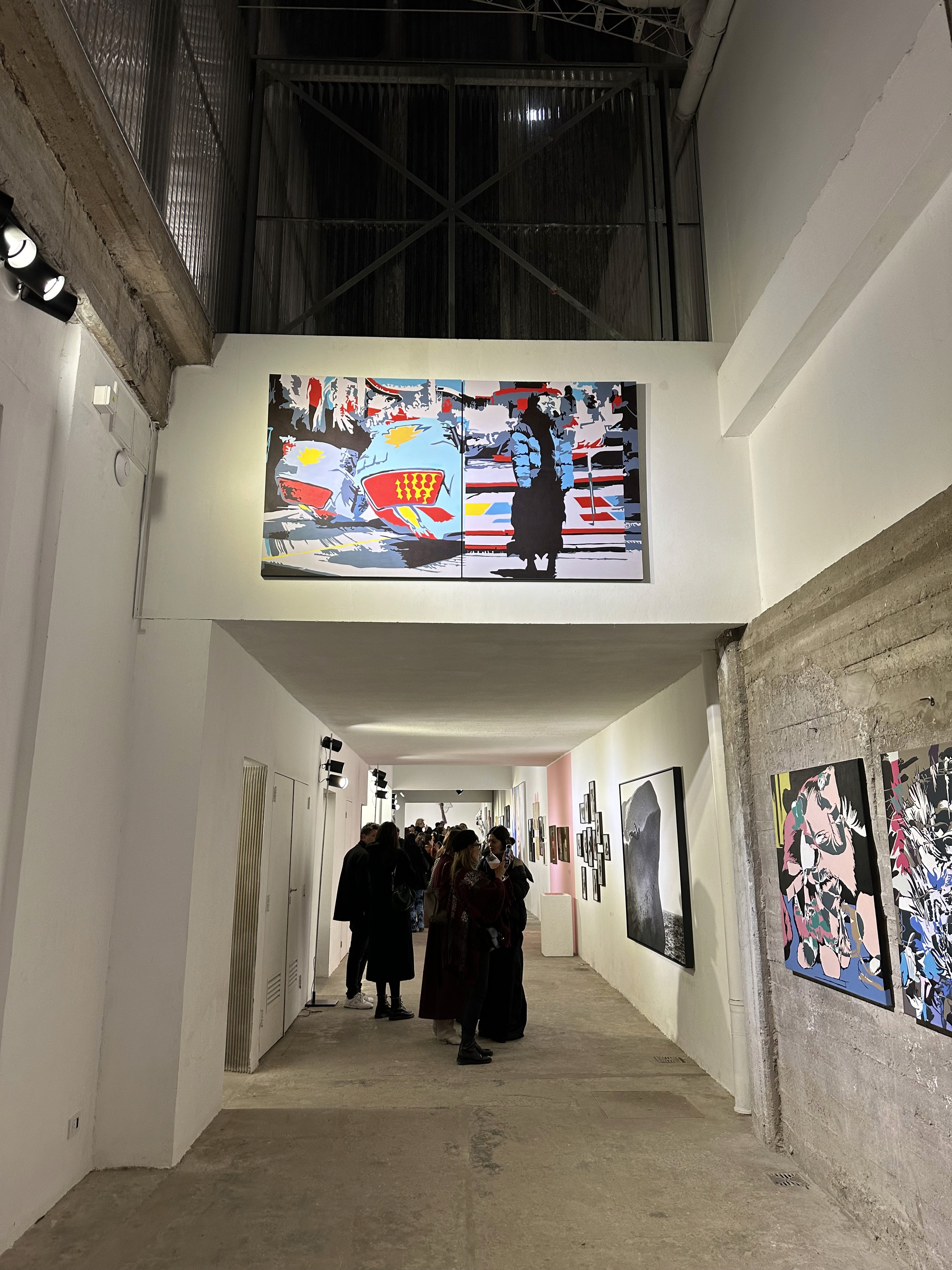 La foto muestra una vista general de una galería de arte con diversas obras en exhibición, destacando un gran bastidor correspondiente a una de las obras del artista KICK.