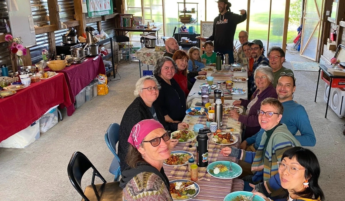 Neighbors and families share a communal meal at a long table inside a farm building at Rooted Northwest.