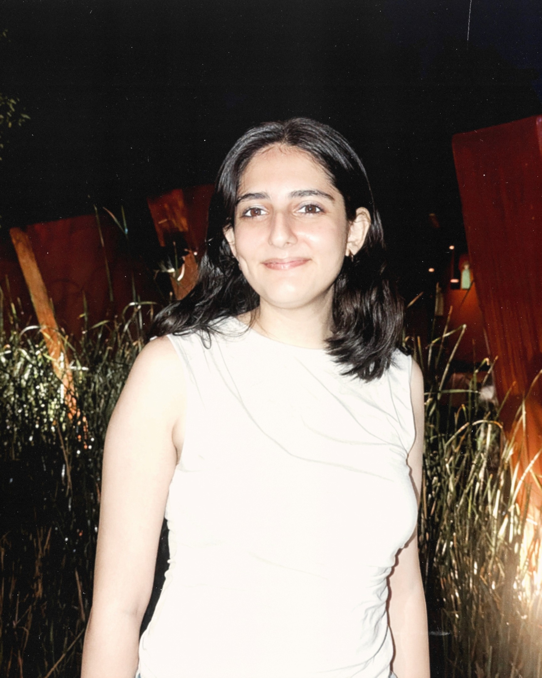 Person wearing a blue puffer jacket and red backpack standing in front of a light blue building on a city street.