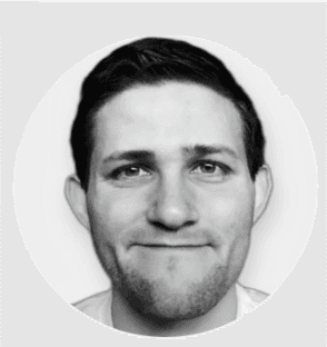 A black-and-white portrait of a smiling individual with short dark hair, wearing a light-colored top, set against a plain circular background.