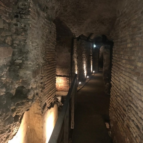 昏暗的古老地下走廊，石墙环绕，狭窄的路径由墙上的灯光照亮。