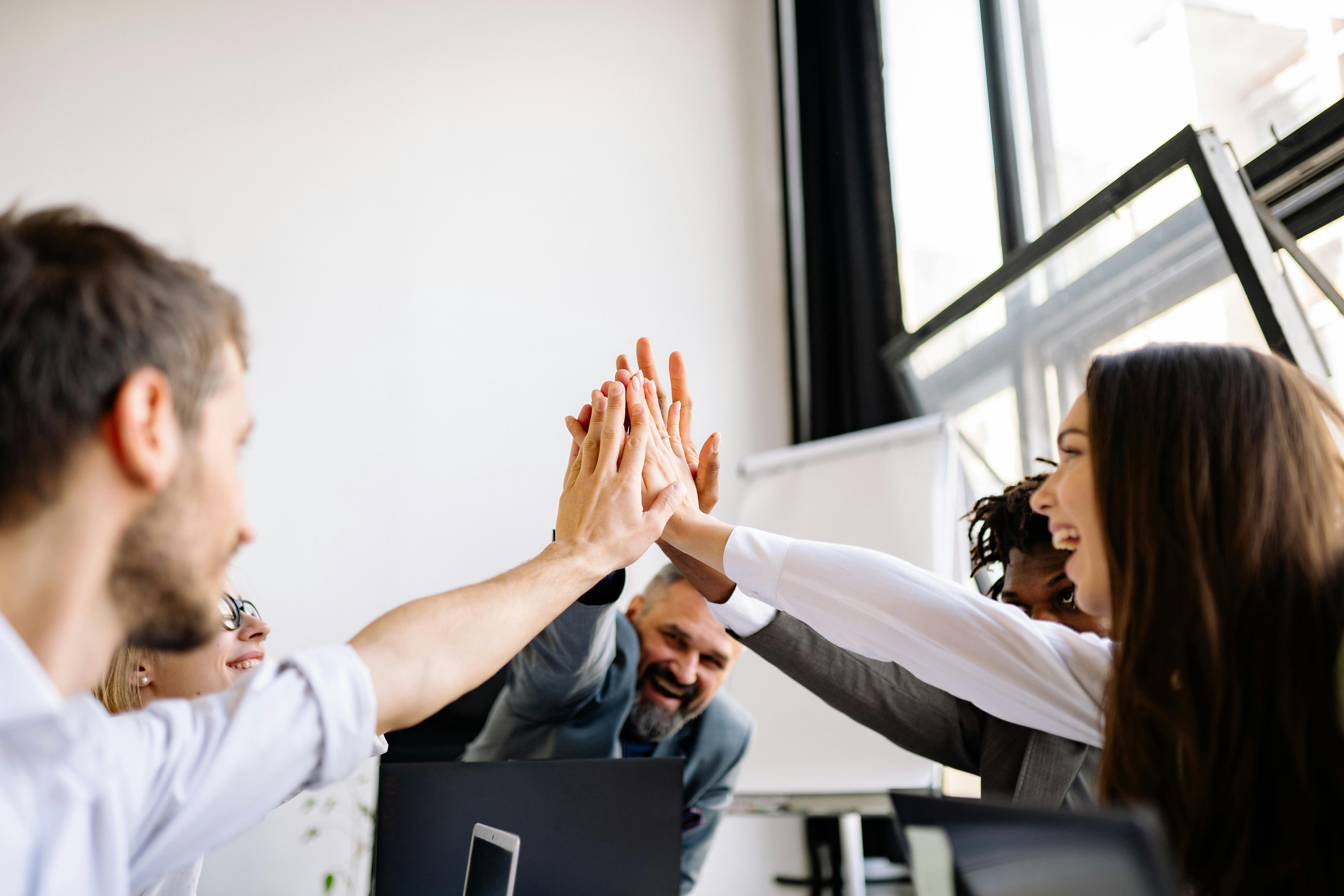 A group of co-workers doing a group high-five with excited looks on their faces
