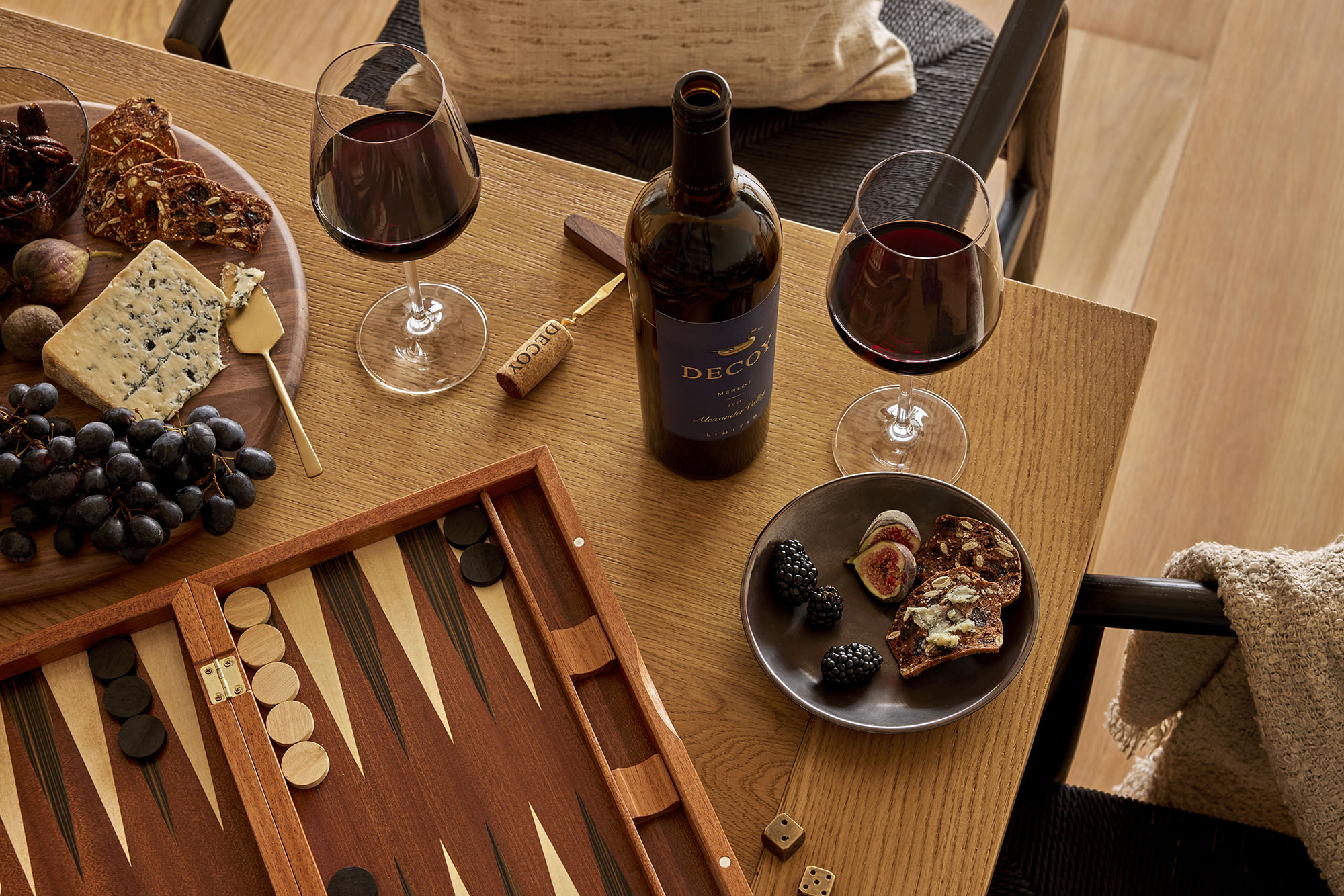 An inviting scene captured from above, showcasing a table set with a wine glass, a bottle of wine, and a plate of grapes. Perfect for a cozy gathering with backgammon and a cheeseboard.