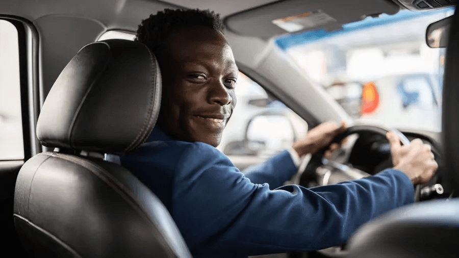 A driver in the car, behind a wheel, smiling and looking at the passanger