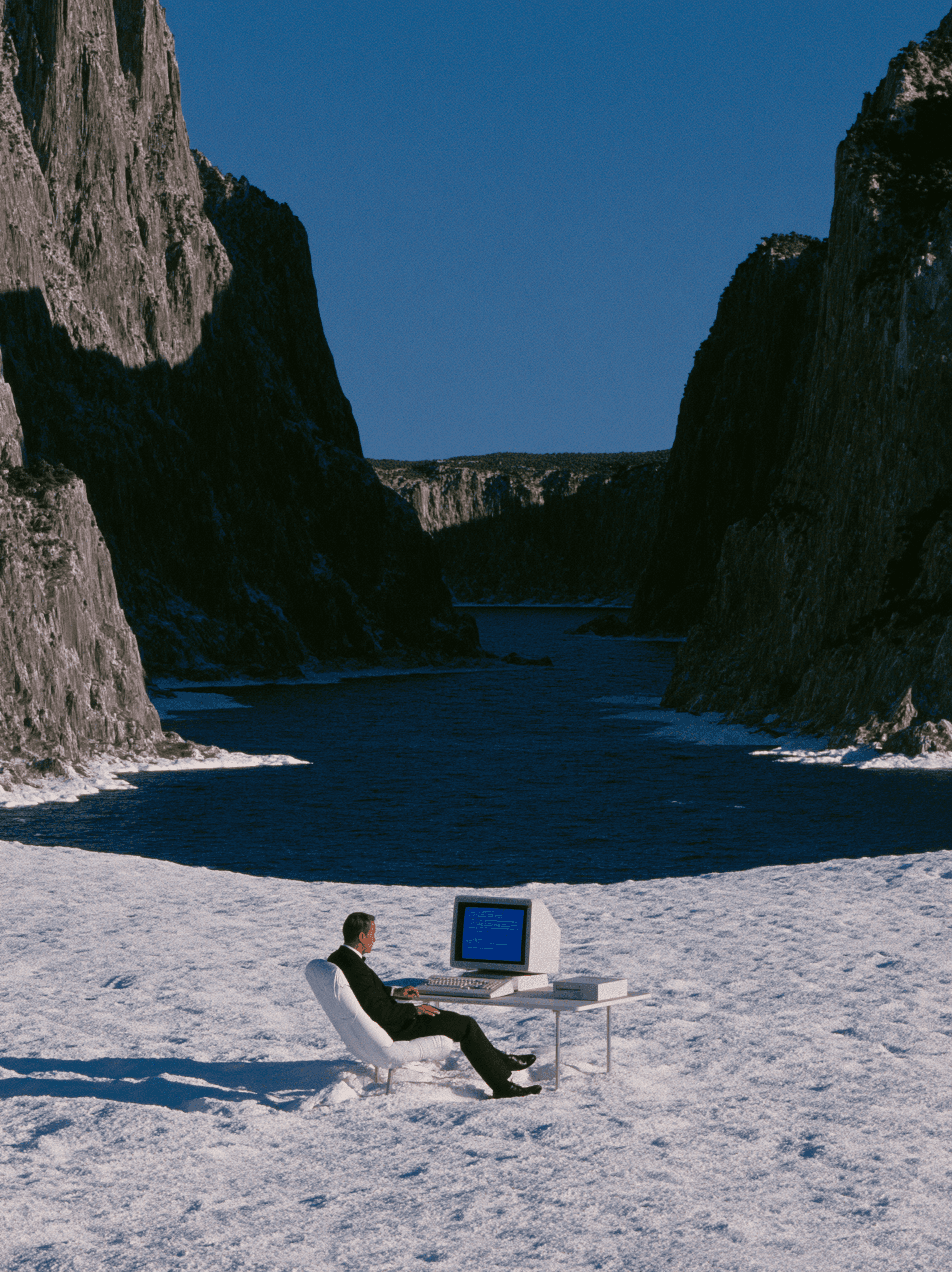 Guy in suit with a computer, sitting on the snow with mountain landscape