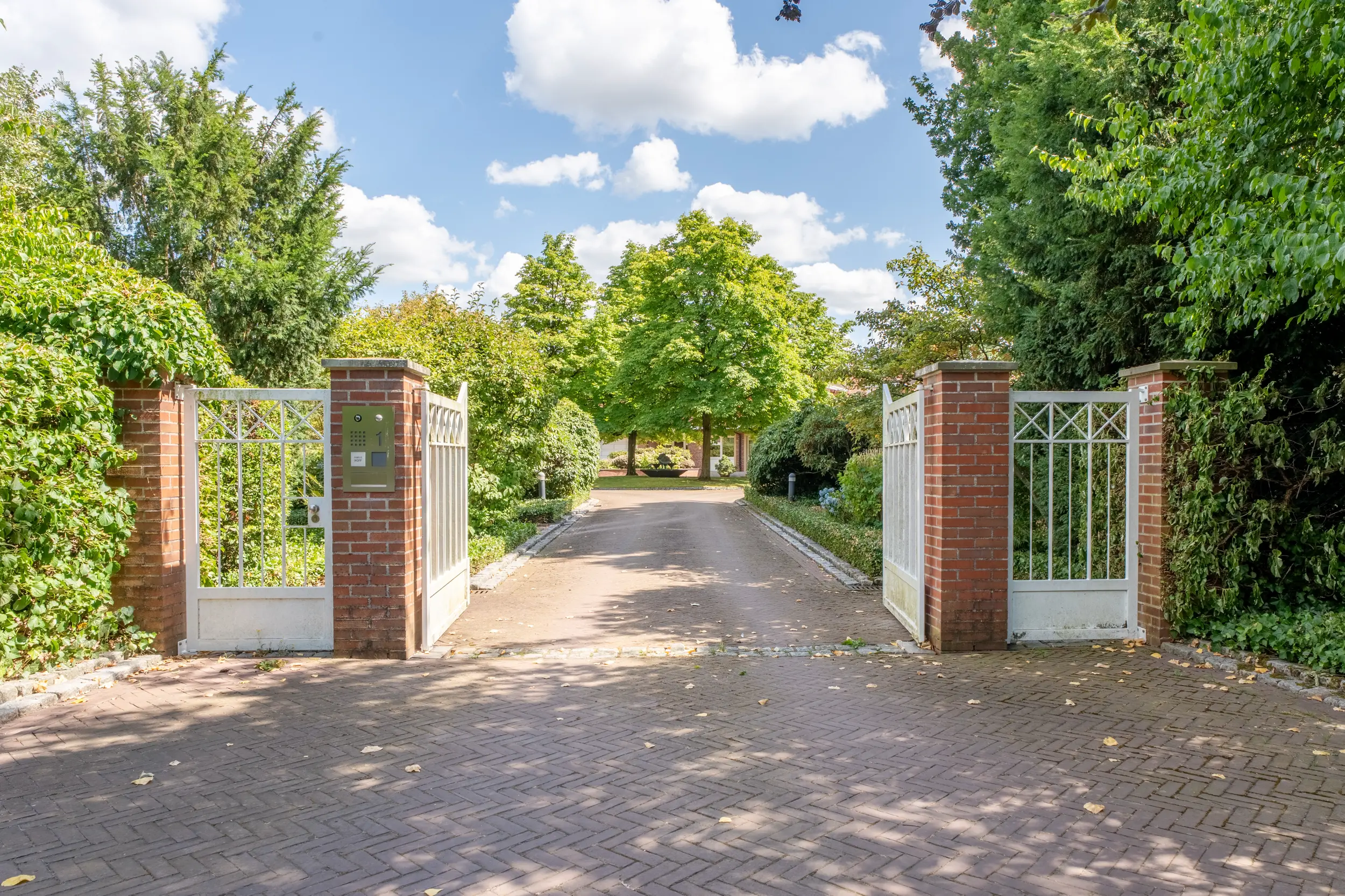 Elegantes Einfahrtstor mit Ziegelpfeilern und weißen Flügeltüren zu modernem Villa in Gronau