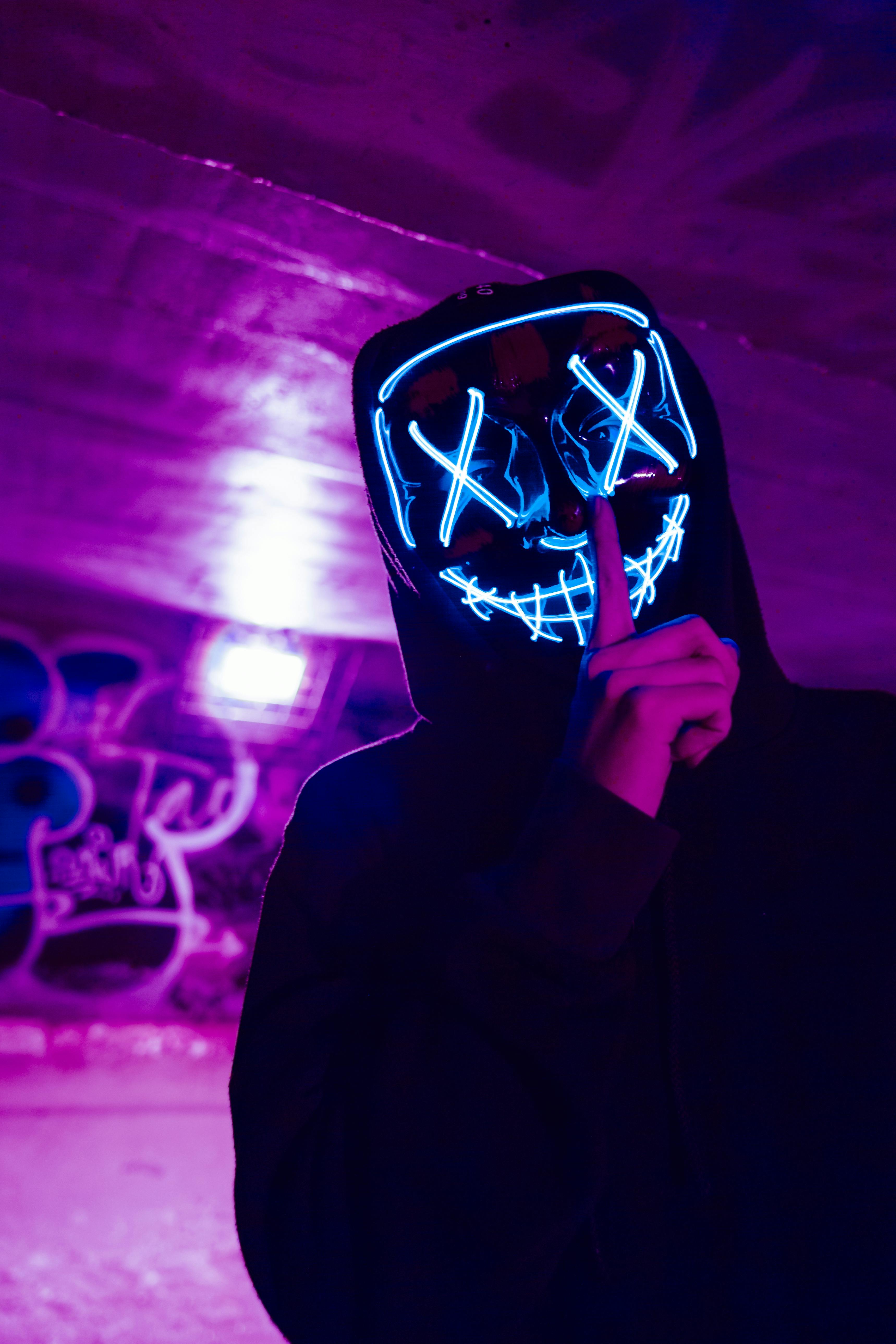 A masked man with index finger over his mouth, implying to be quiet.