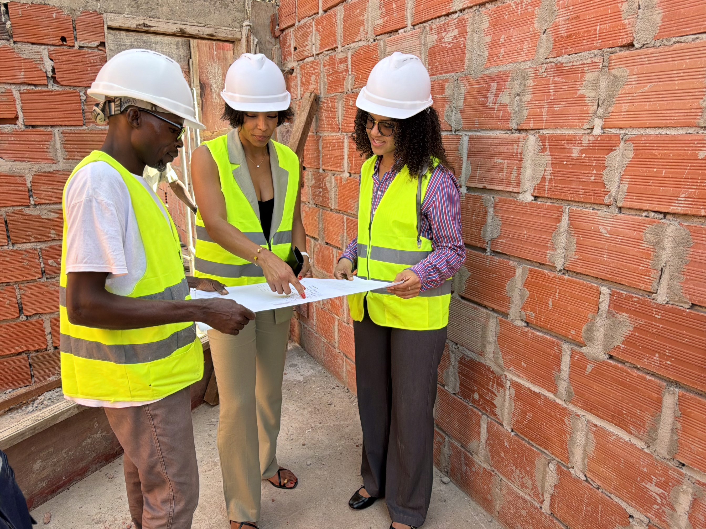 Construction site with four workers in safety vests and helmets. They stand on a large concrete foundation with rebar grids and blue tarps, communicating and planning.