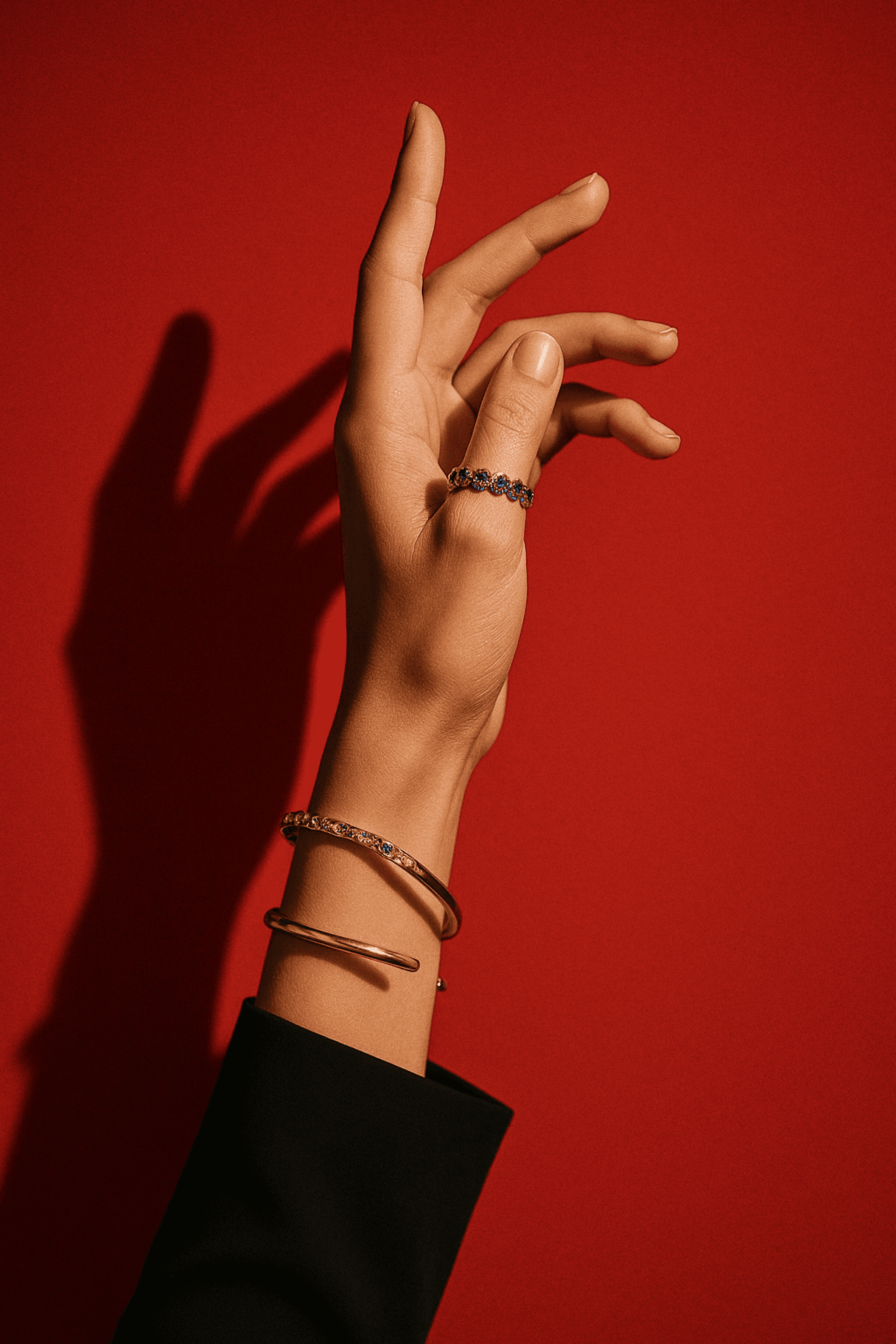 Elegant hand against a red background wearing two gold bracelets, one sleek and minimal, the other a delicate chain.