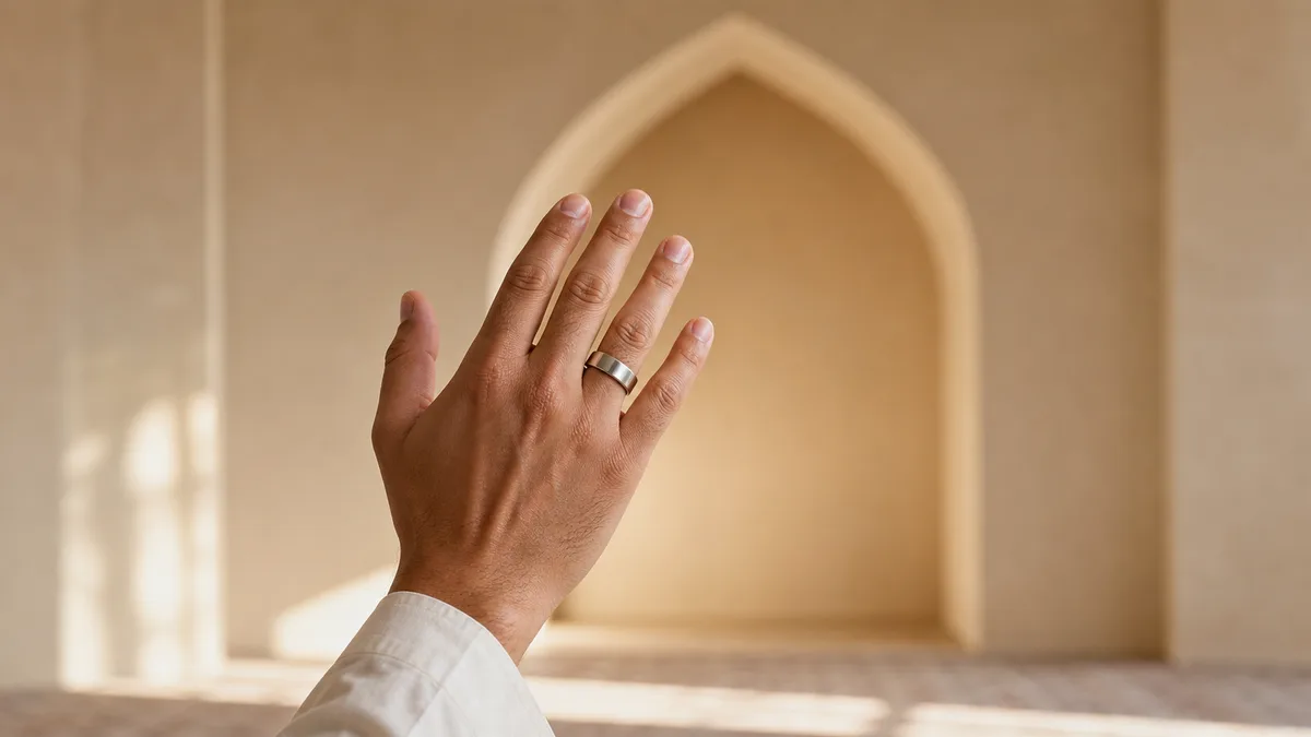 Hand wearing a smart tasbih ring before a plain mihrab arch in warm light