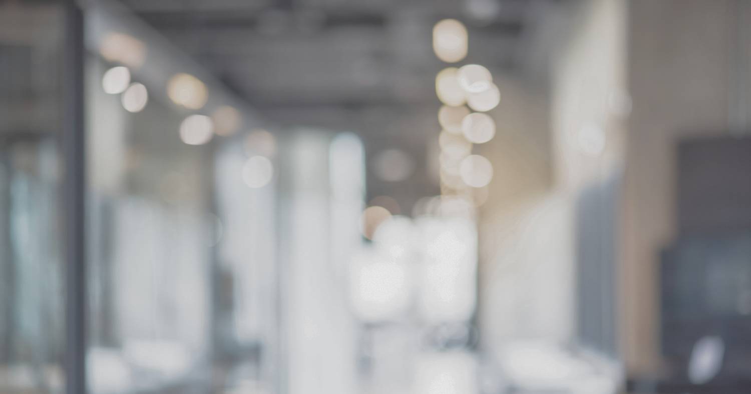 Unscharfes Bild eines modernen Bürogebäudes mit Glaswänden und heller Beleuchtung. Die Aufnahme vermittelt eine professionelle, ruhige und zeitgemäße Arbeitsatmosphäre.