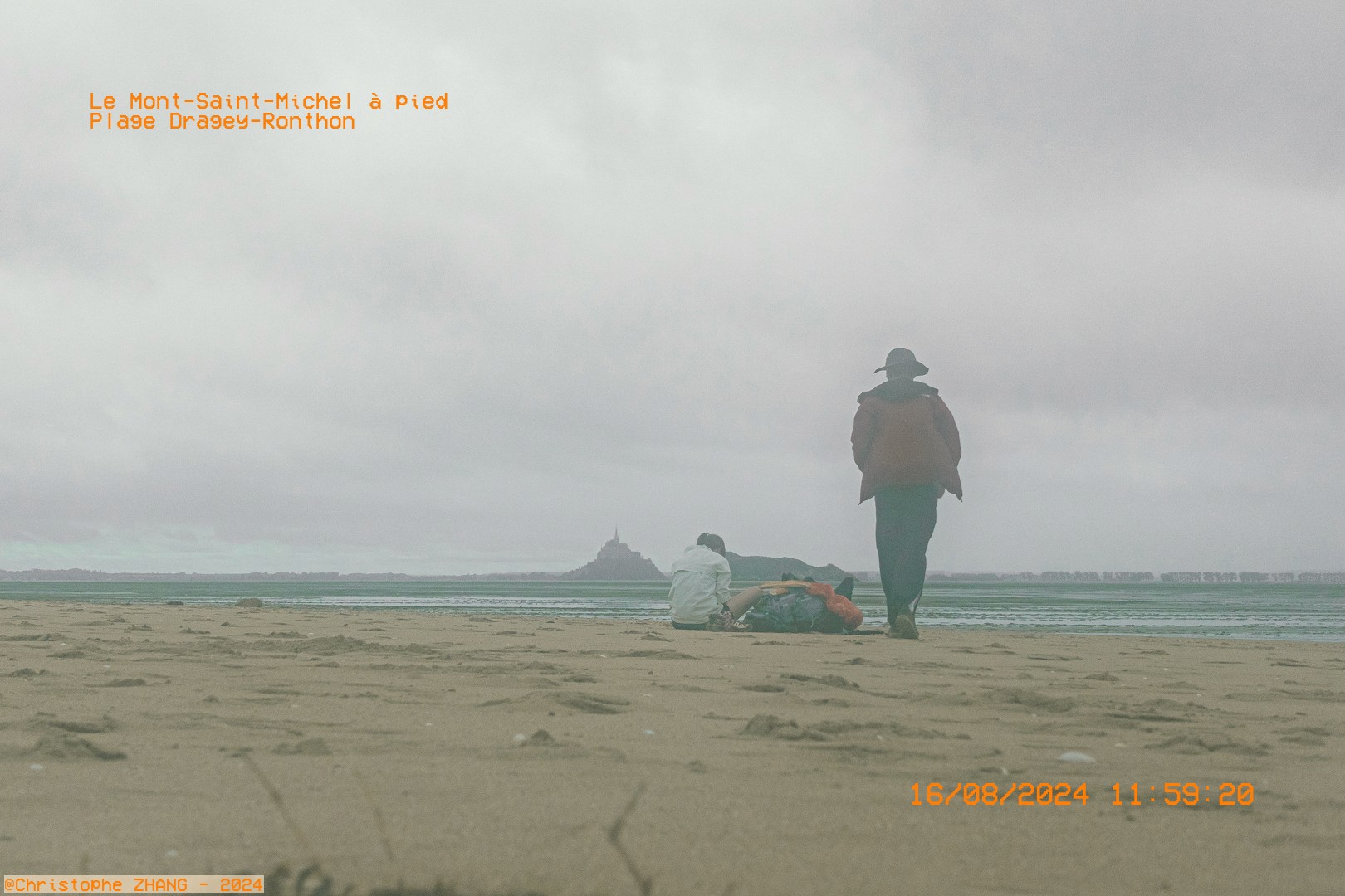 Promeneurs sur la plage de Dragey-Ronthon, avec le Mont-Saint-Michel visible dans la brume.