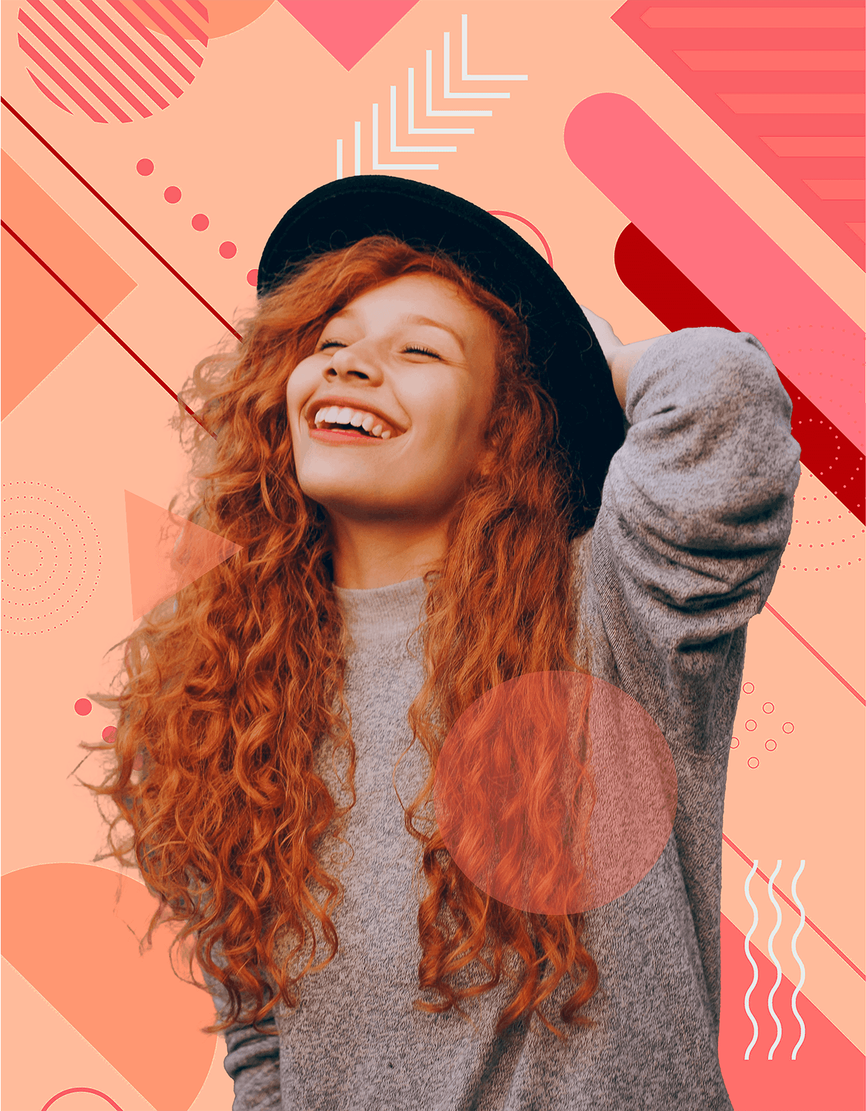 A woman with curly red hair and a black hat smiles, holding her hair back.