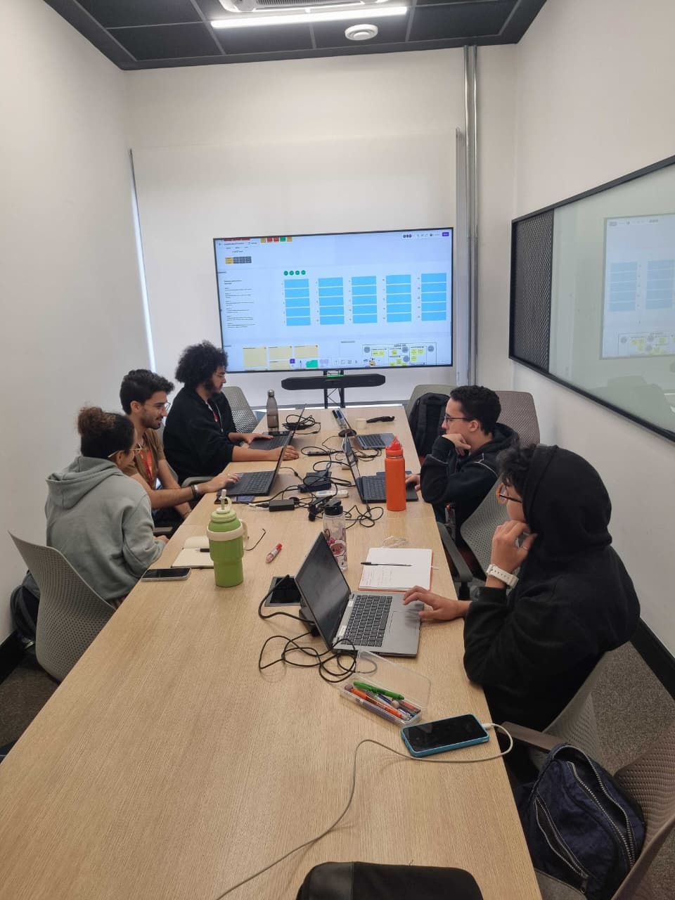 A group of students working on a rooom, using notebooks and a television as monitor.