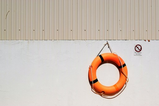 An orange life preserver is hanging on a white wall, with a small round object above it.