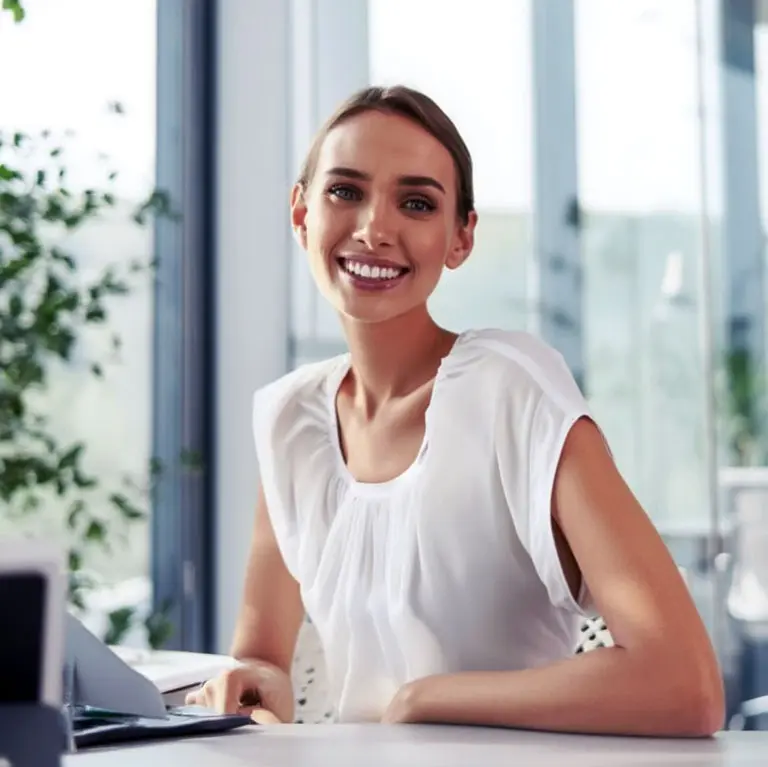 Smiling businesswoman in white shirt at desk. Professional office setting.