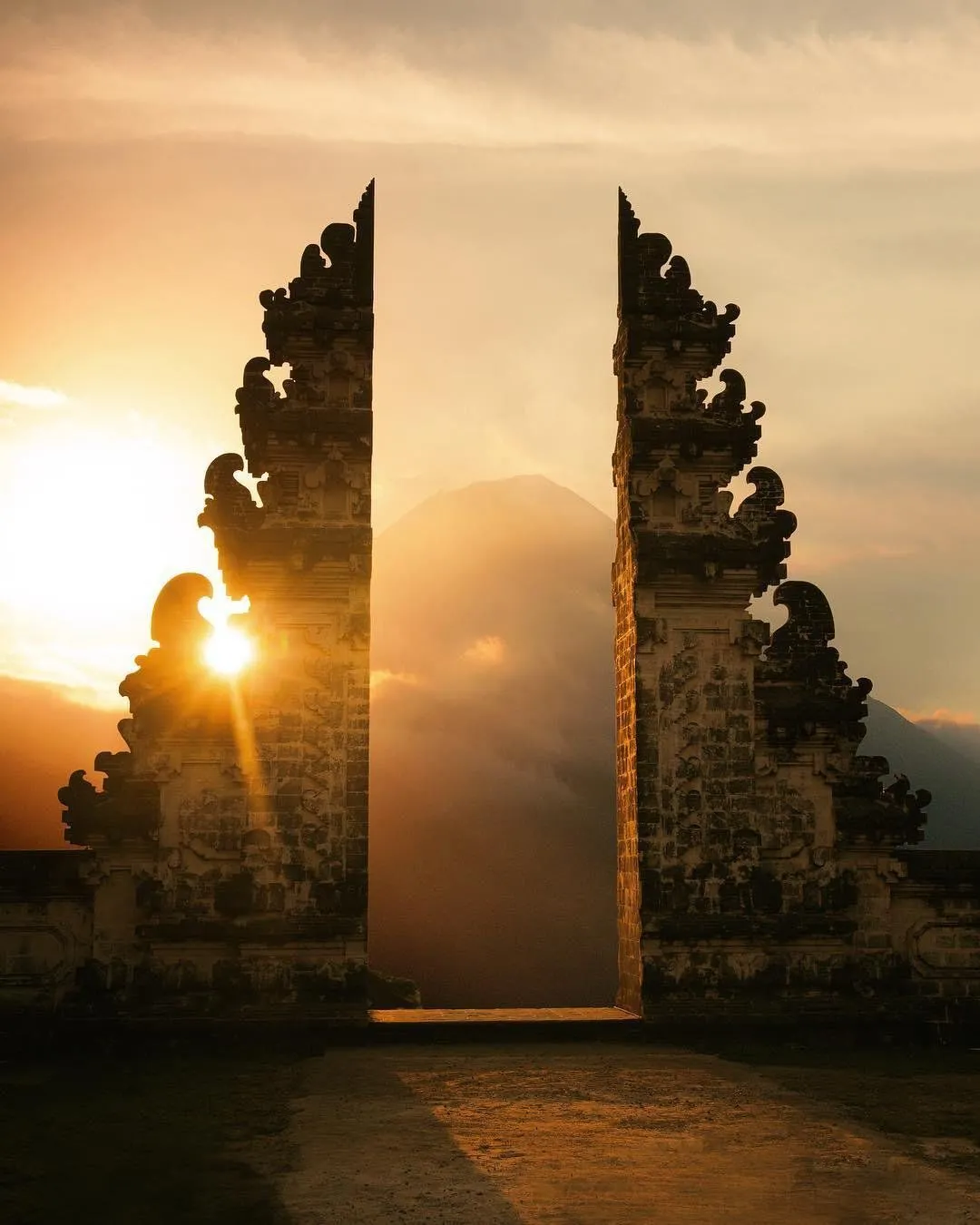 Temple gate in Bali at sunrise, with sun rays and mountain peak