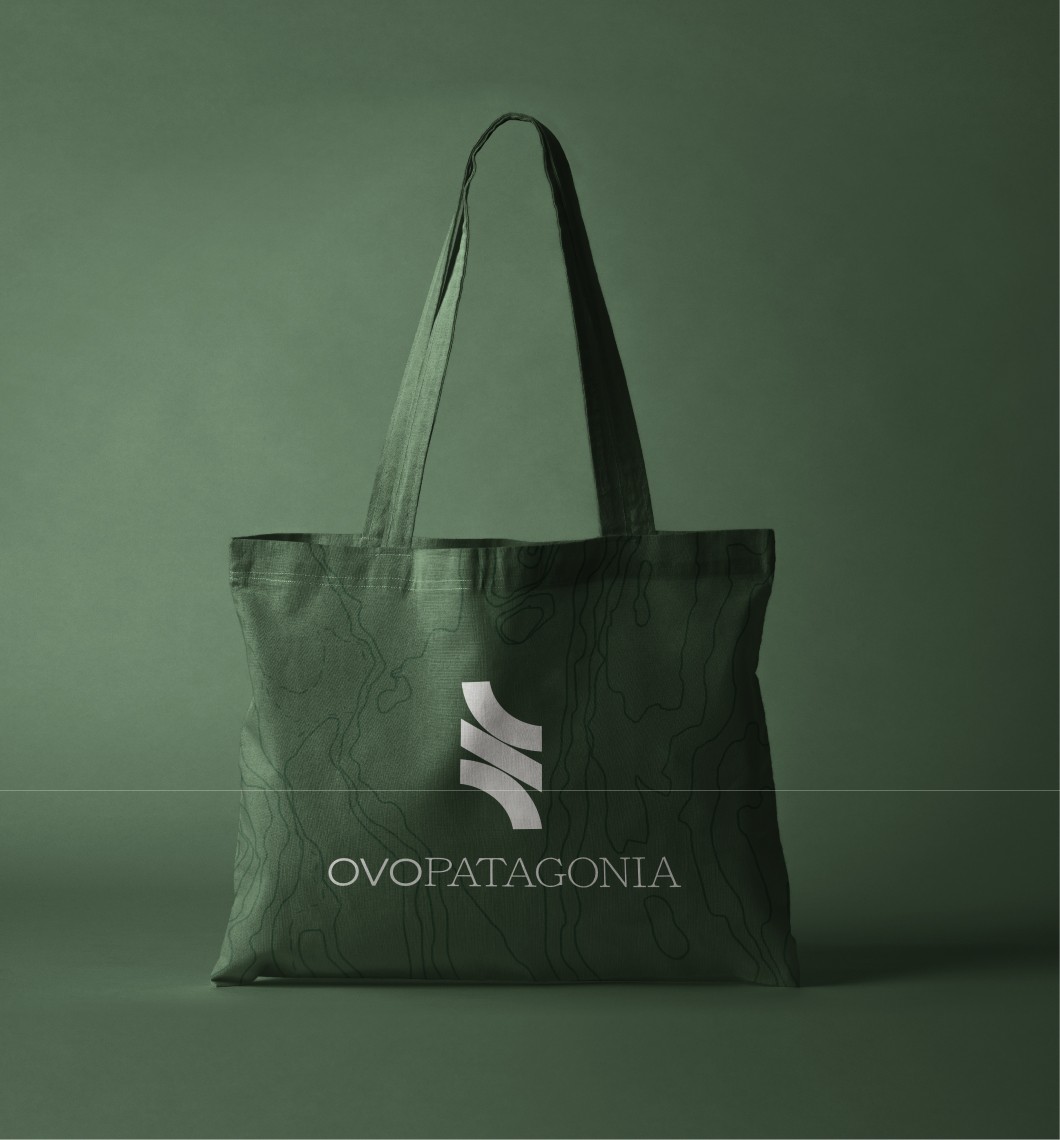 Bolsa tote verde con patrón topográfico y logo curvo; texto “OVOPATAGONIA” blanco centrado, fondo verde uniforme.