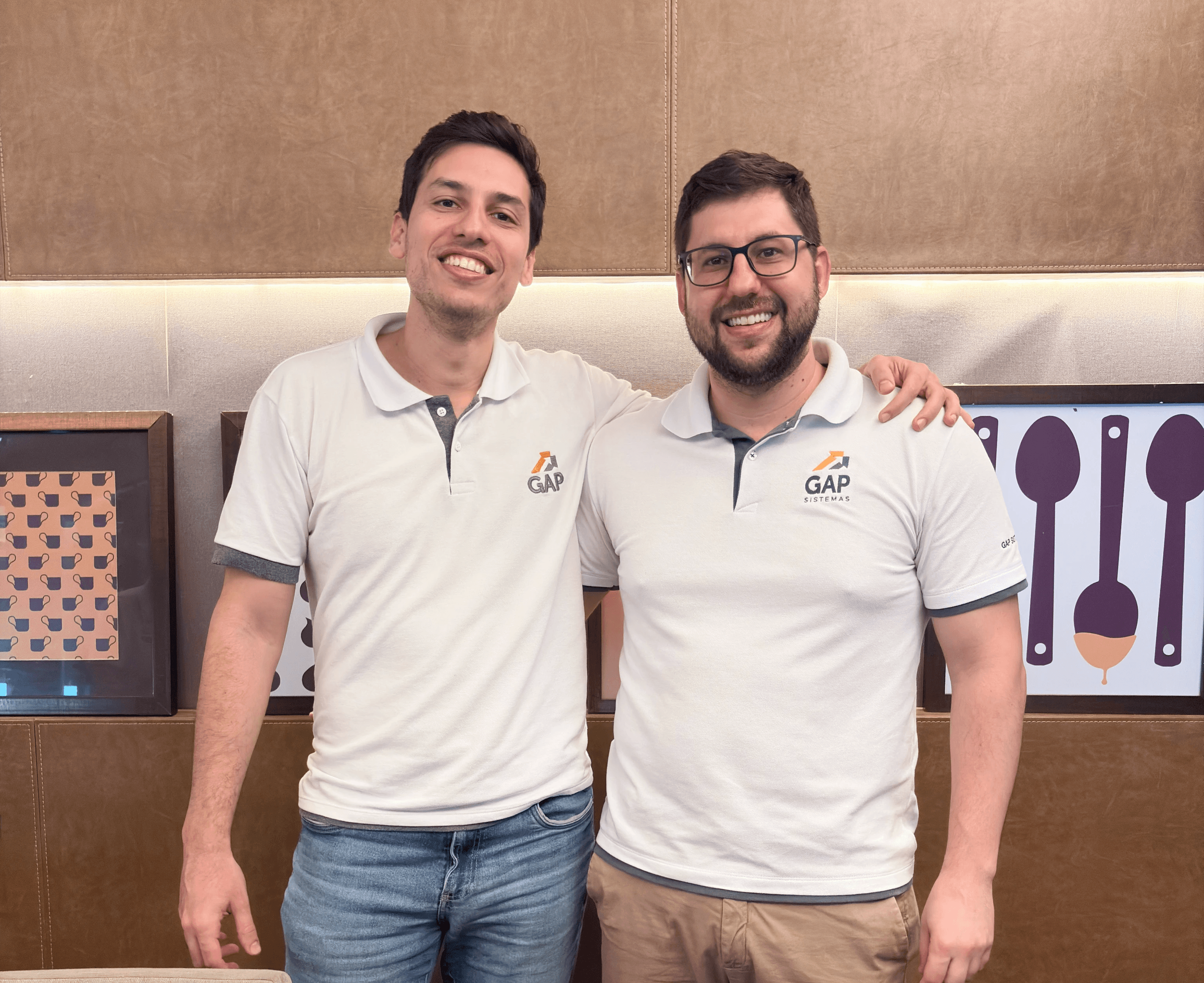 Quatro membros do time da GAP Sistemas, vestindo camisas polo brancas com o logo, sorrindo e posando no stand da empresa em um evento, com o logo da GAP ao fundo.