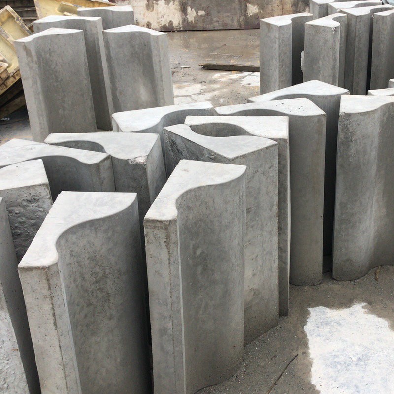 A group of large, grey concrete blocks with curved surfaces, arranged in a random pattern on the ground. These blocks are designed with a wave-like profile for architectural or construction purposes.