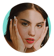 Close-up portrait of a woman with her hands on her face. She has brown hair and is wearing white nail polish.