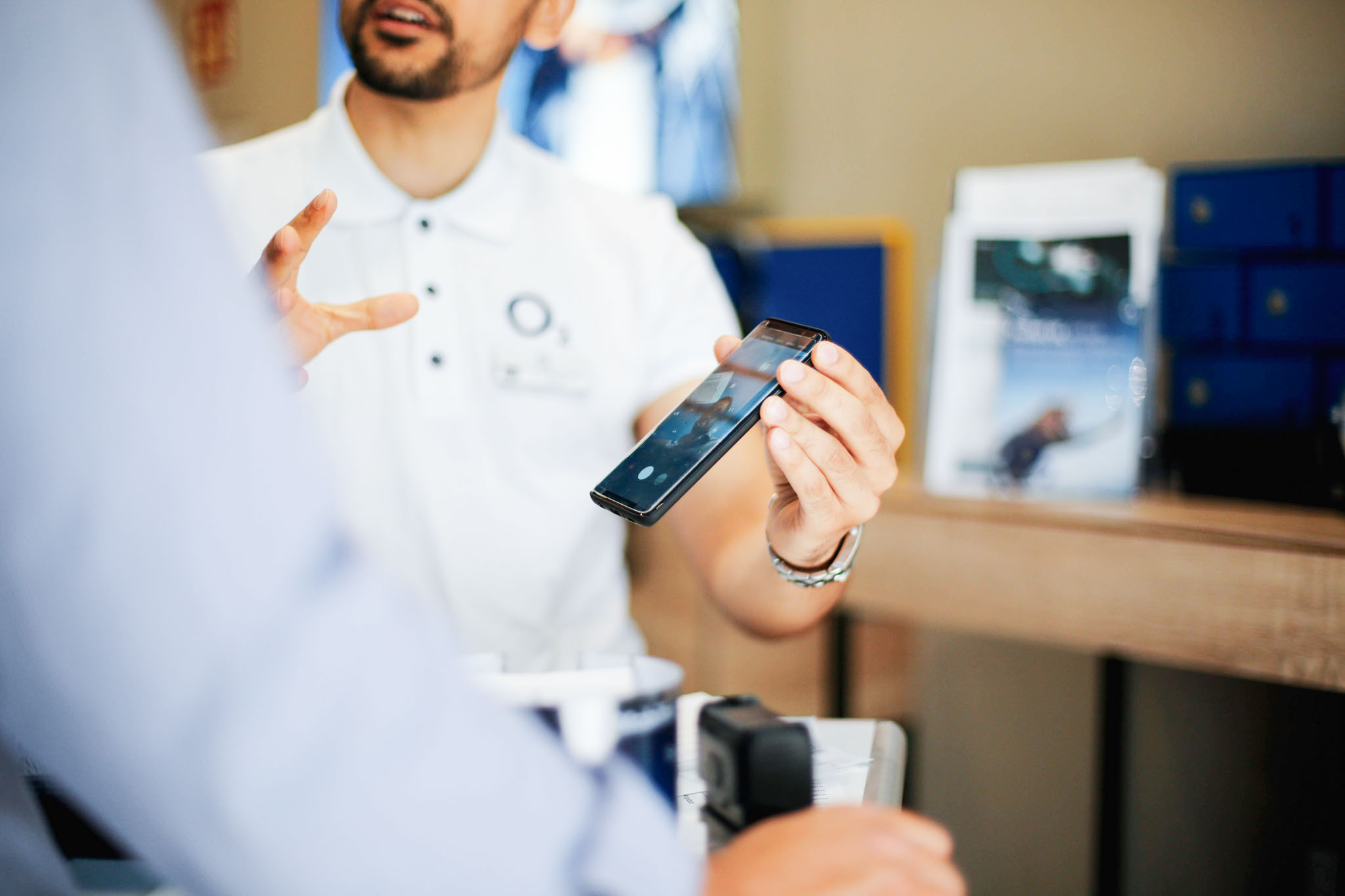 Promoter zeigt einem Kunden ein Smartphone in einem modernen Shop-Umfeld. Die Telco-Branche verbindet technische Beratung mit maßgeschneiderten Produktlösungen.