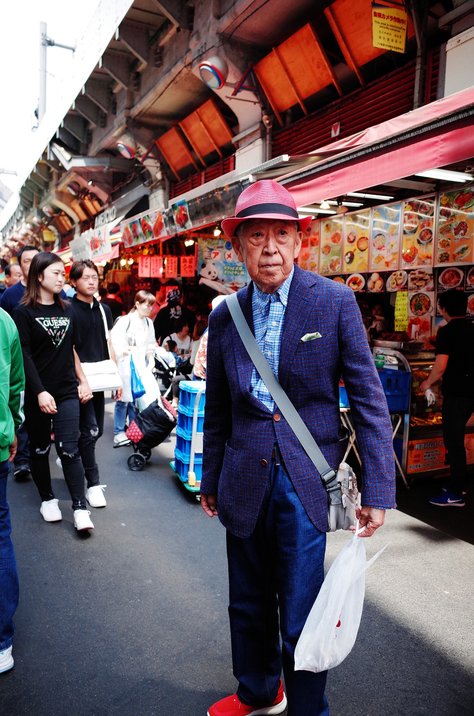 Portait d'un vieil homme japonais habillé de manière chic avec un costume en laine violet et un chapeau rose et des chaussures rouges se tenant debout en pleine rue lors commerçante dans un marché ouvert japonais dans le quartier de Ueno à Tokyo