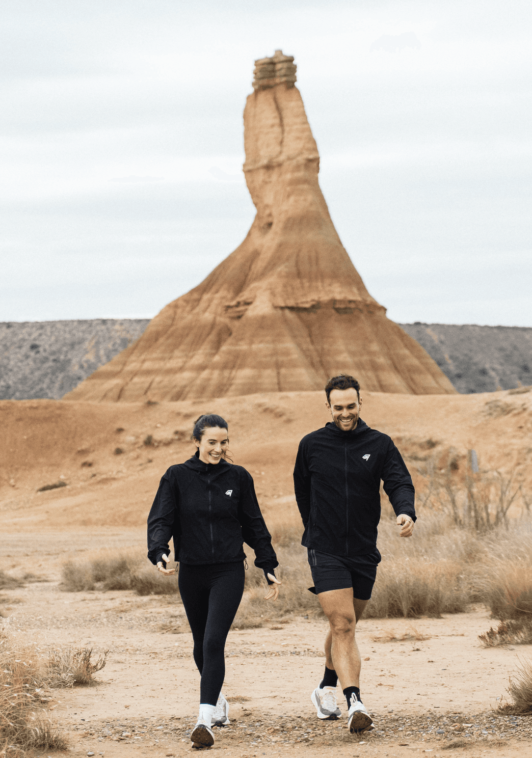 Man wearing olive green and orange sneakers with tall socks, standing on an urban street with a modern fence and skyscraper in the distance.