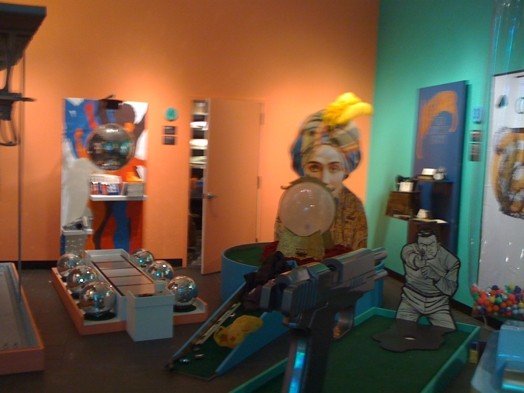 installation view of sculptures made of different materials and in different shapes, a disco ball, a crystal sphere, and a mini-golf course, etc