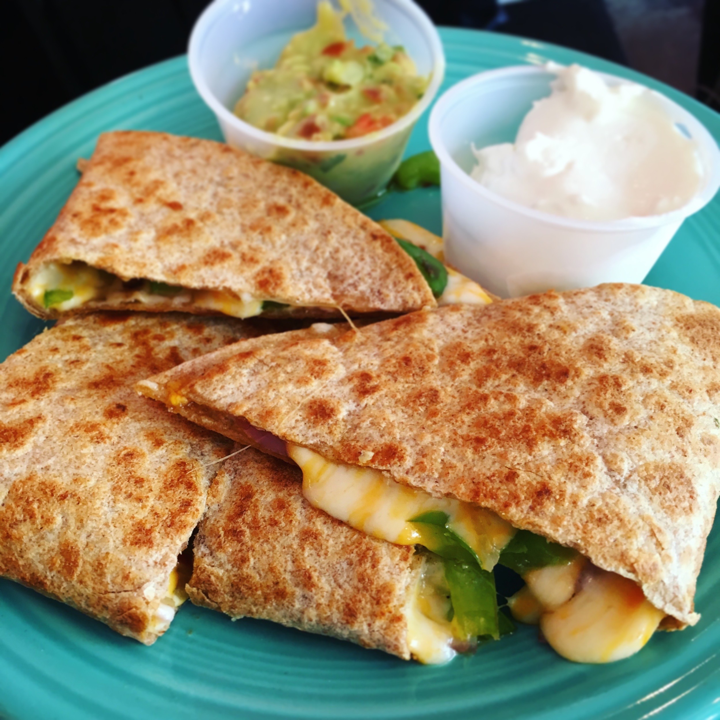 A crispy, golden-brown quesadilla from Taco Spot LA, filled with gooey melted cheese and tender carne asada, served with fresh guacamole and sour cream on the side.