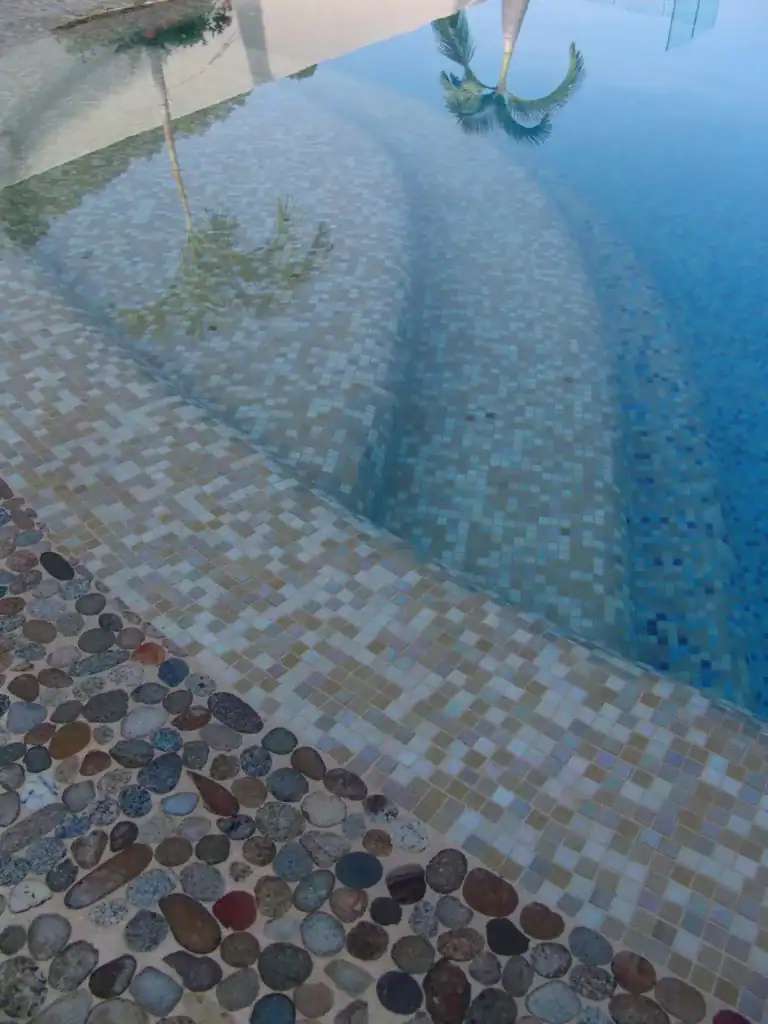 Pool floor in a blue-grey glass blend meeting a river rock border — Mosaiclegs Art Studio
