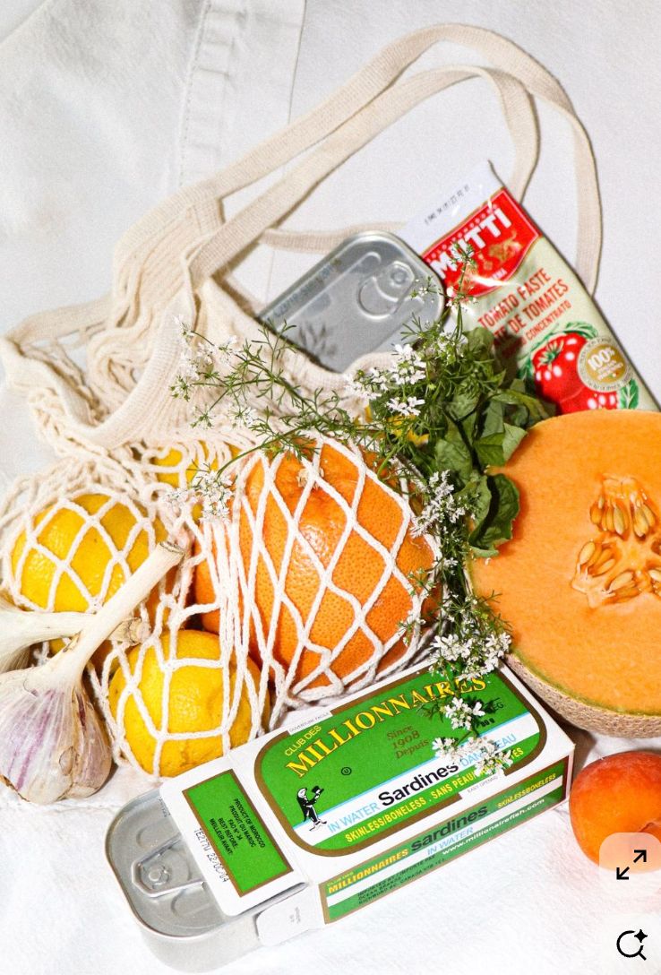 White plate with roasted chicken served in a golden sauce with herbs and capers, placed on a terrazzo tabletop in sunlight.