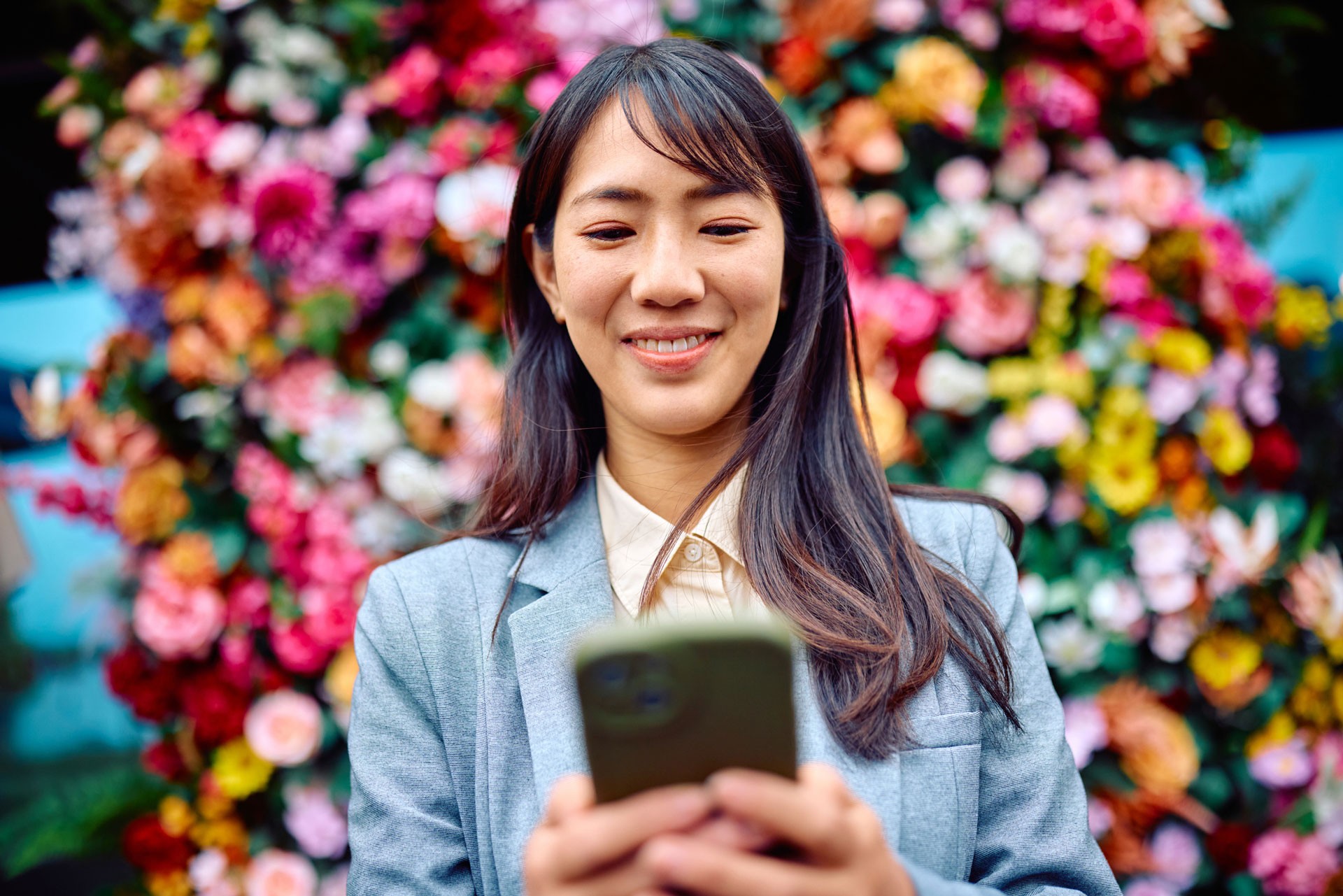 woman with mobile phone smiling with colorufl flowers at the background