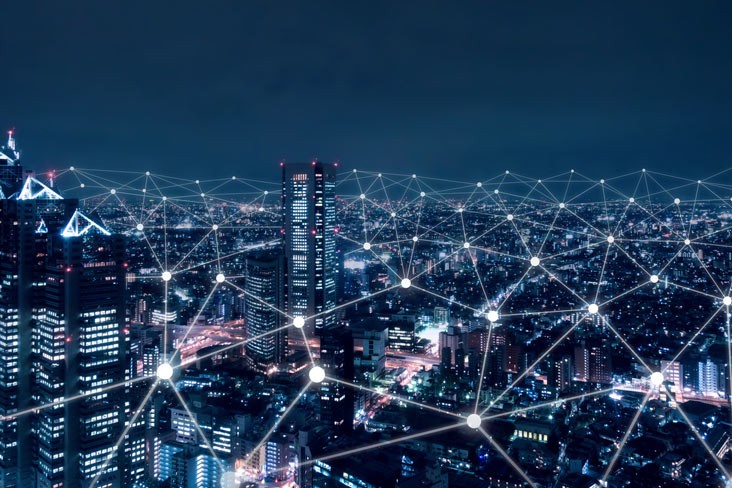 A person walks in front of large stone arches with dark doors, flanked by tall columns, in a historic building.
