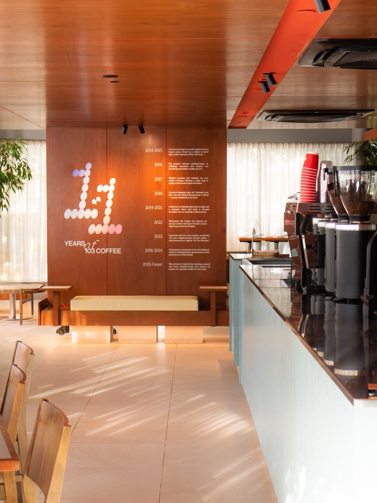 Interior of 103 Coffee showcasing a seating area with wooden benches, a coffee counter, and a wall displaying '11 Years of 103 Coffee' with a timeline of milestones.